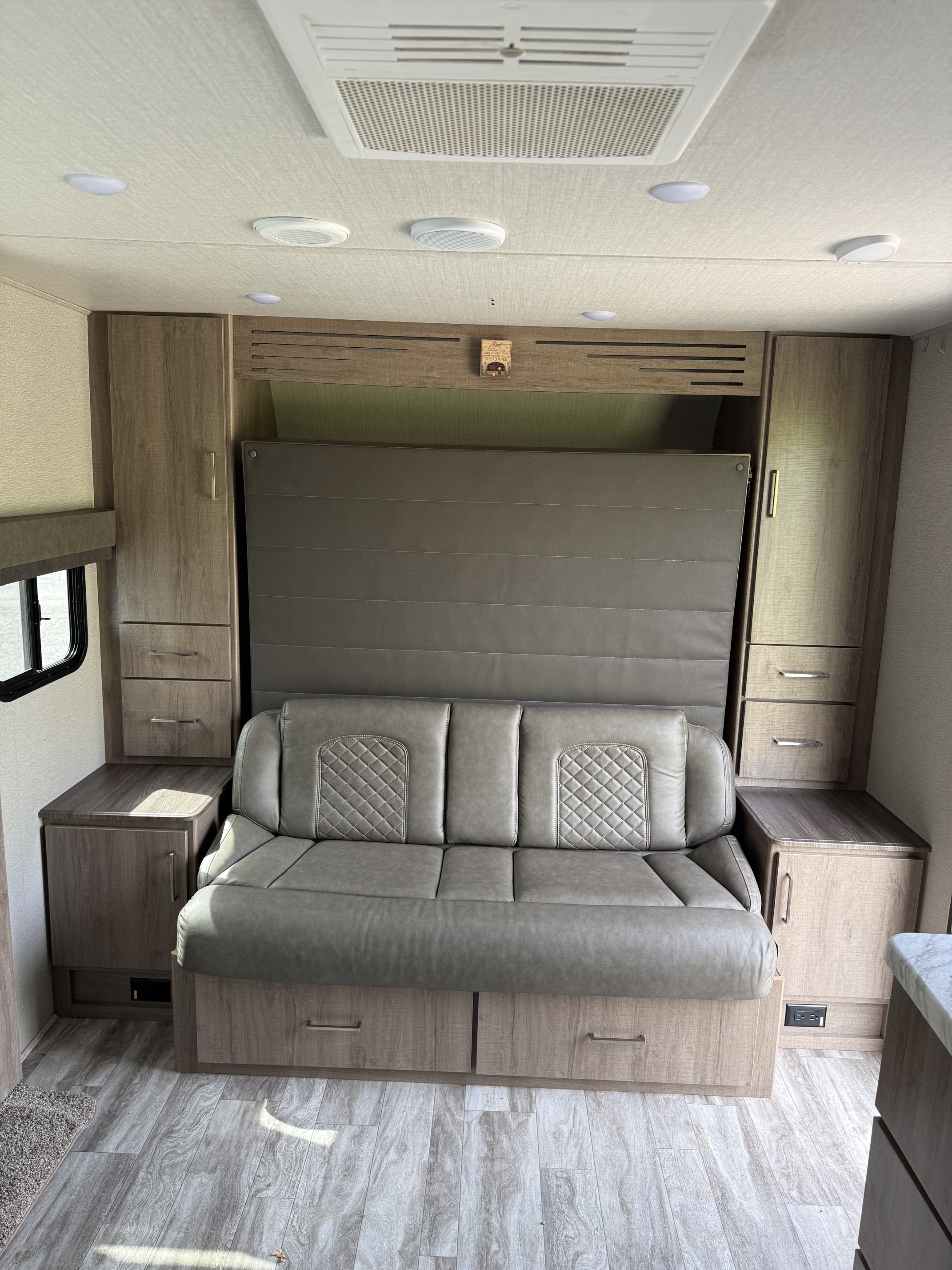 Cozy RV rental interior: gray sofa/murphy bed, wood storage cabinets, AC, and lights create a functional living space.. Grand Design Imagine XLS 2022