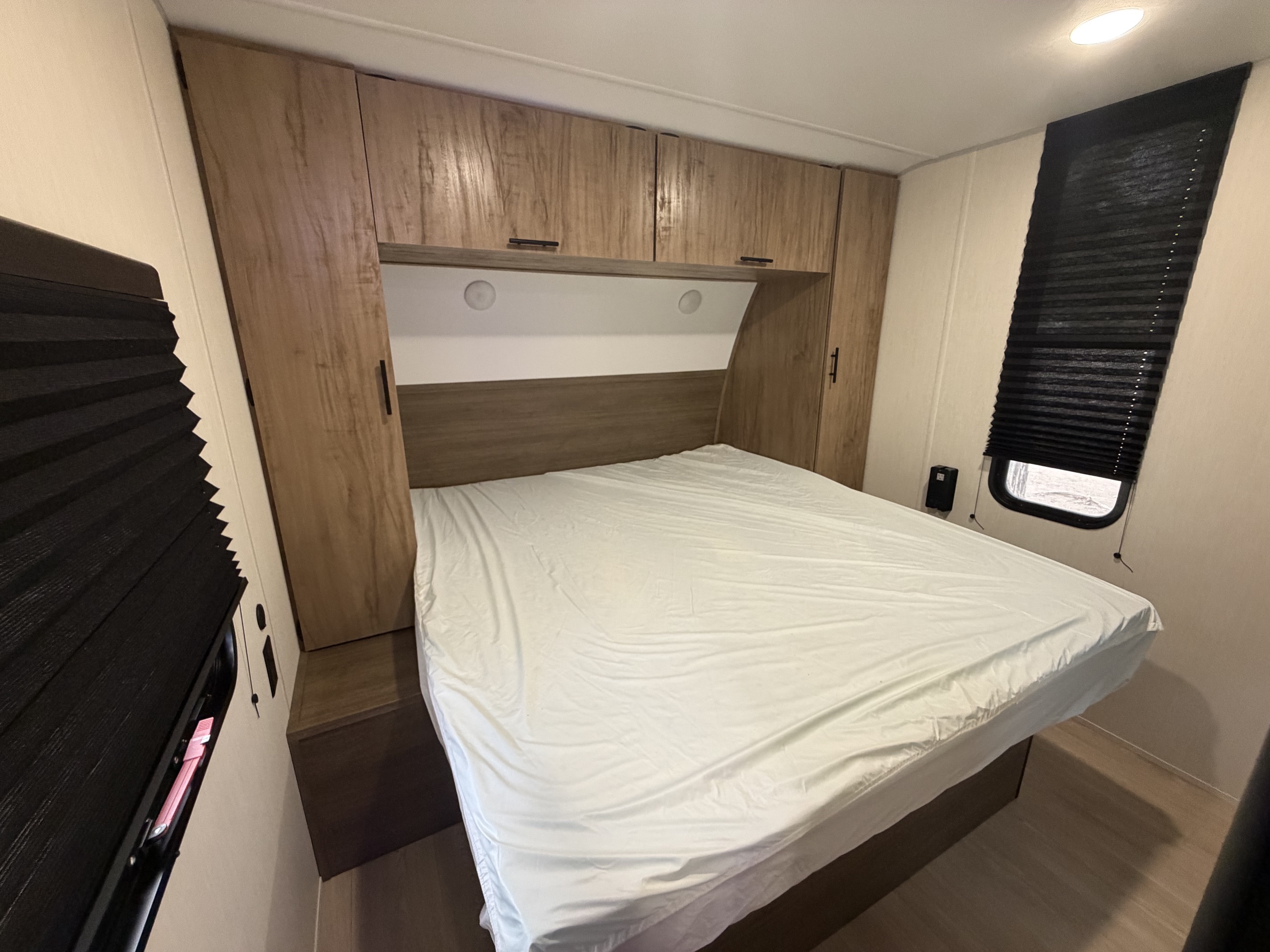Cozy RV rental bedroom featuring a white bed, wood cabinets, and dark blinds for privacy and comfort on the road.. Forest River Cherokee Grey Wolf 2025
