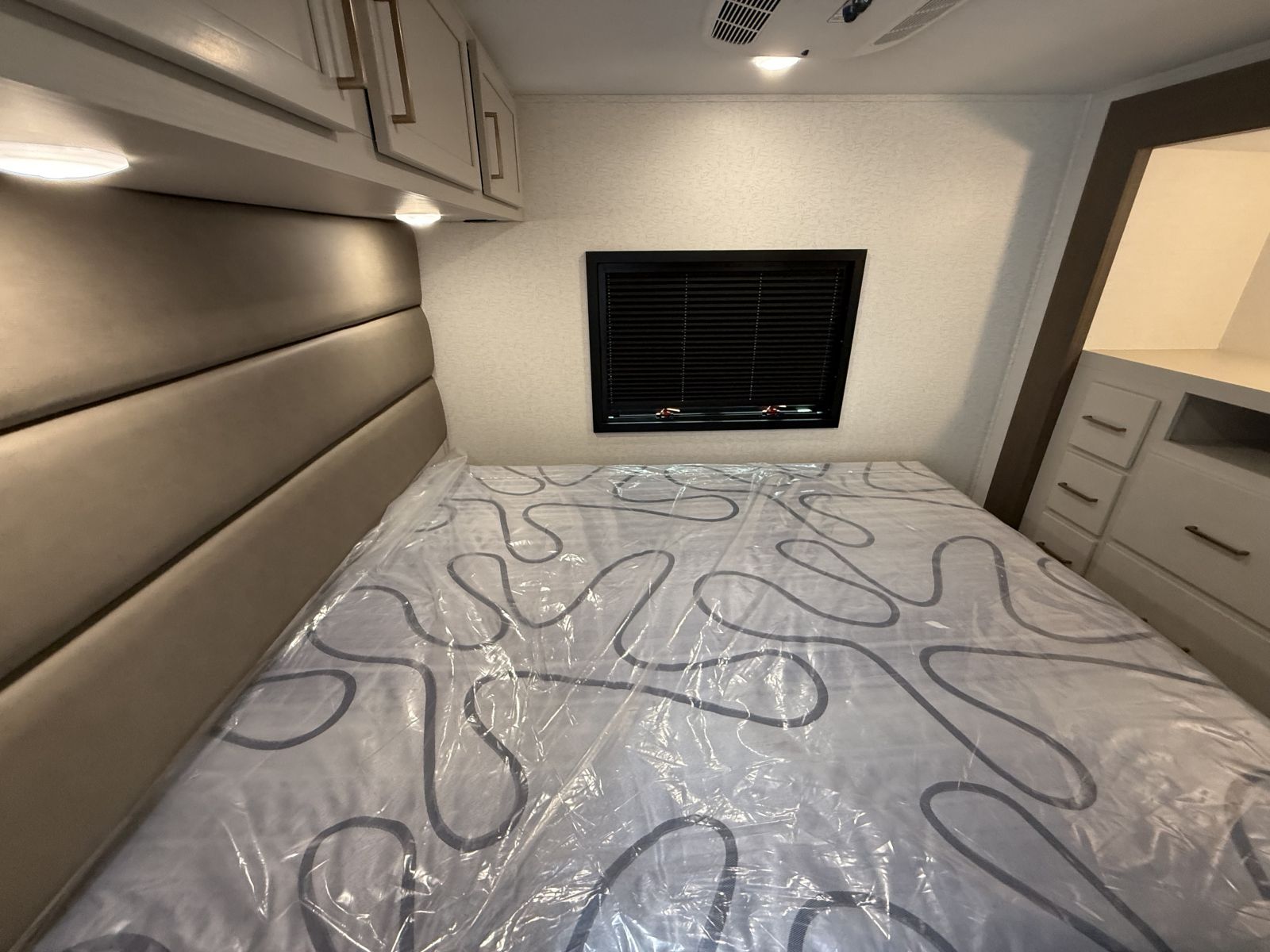 RV rental bedroom: New bed with plastic wrap, padded headboard, overhead storage, window with blinds.. Forest River Other 2027