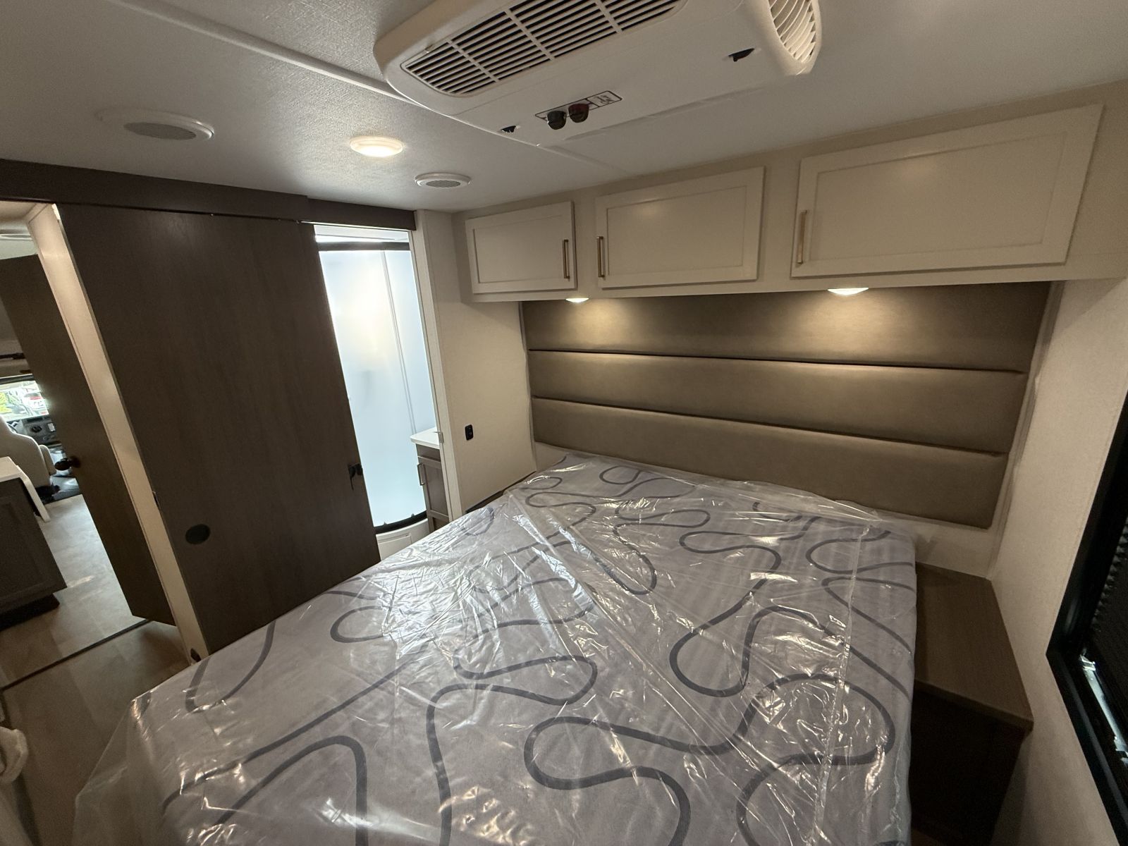 Spacious RV rental bedroom featuring a comfortable bed, padded headboard, overhead cabinets, and a sliding door to the bathroom.. Forest River Other 2027