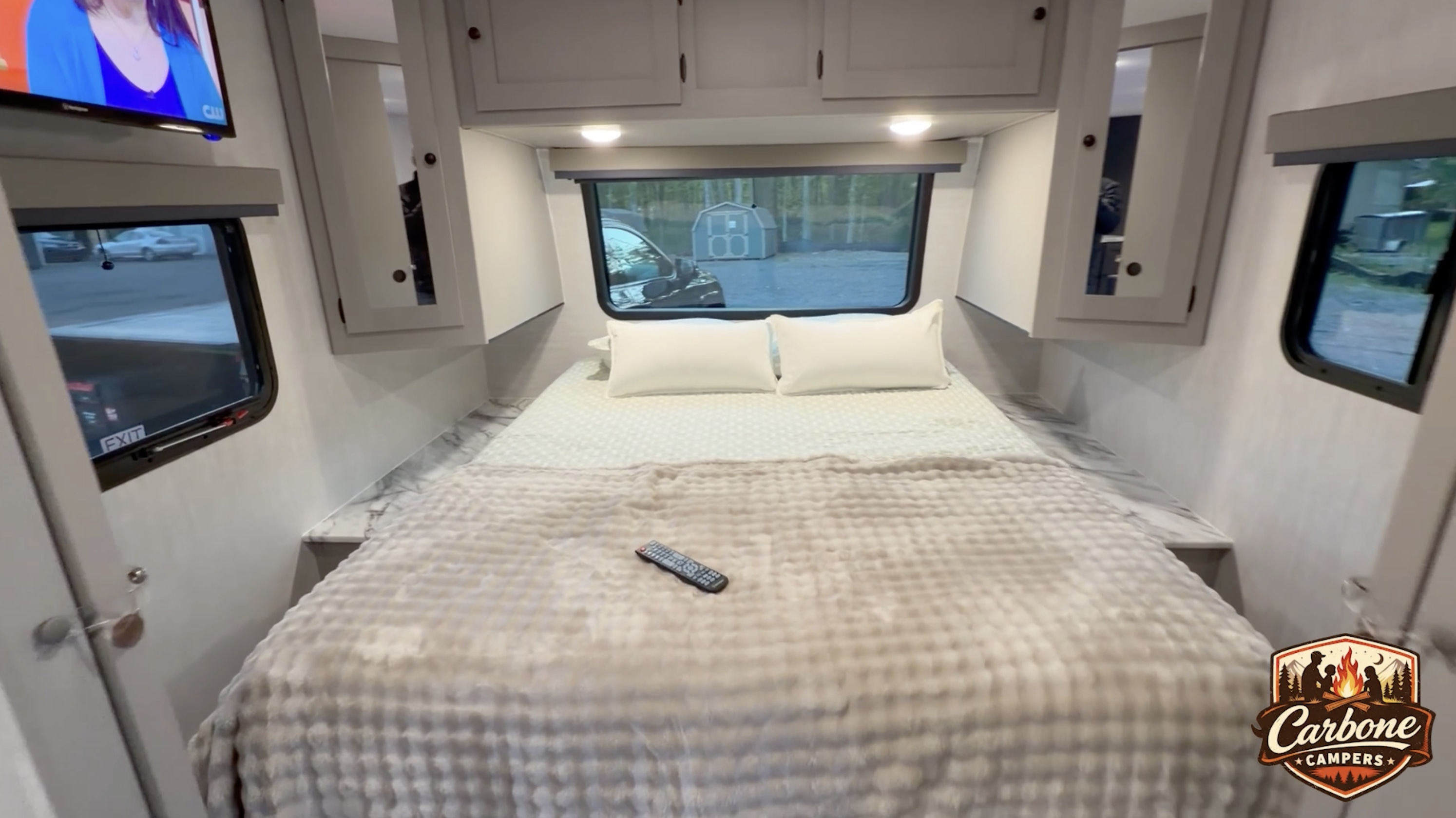 Spacious RV rental bedroom featuring a comfy bed, TV, and overhead storage. Outside the windows, a car and shed are visible.. Coachman Apex 300BHS 2026