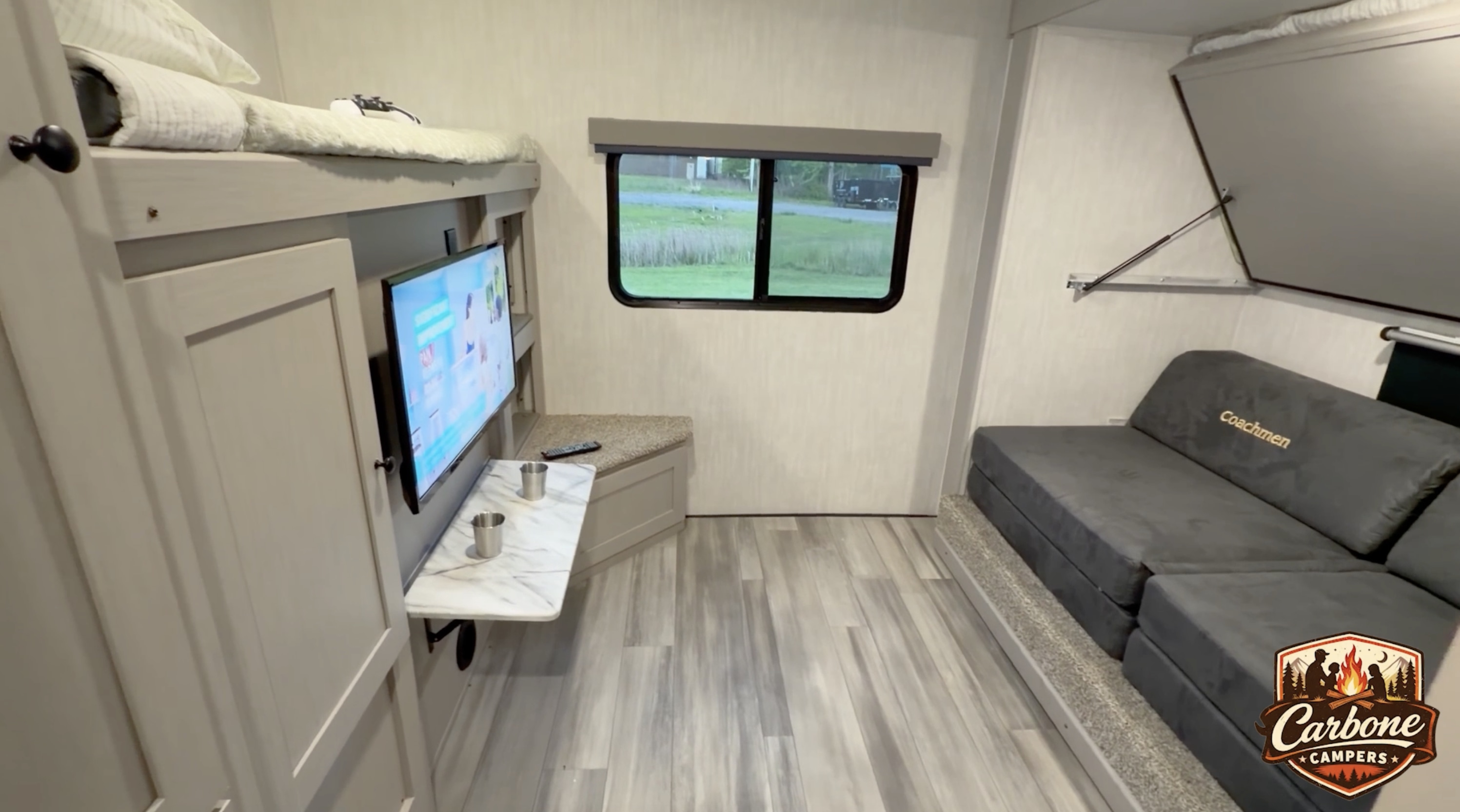Inside an RV rental: bunk beds, mounted TV with a pull-down table, an outdoor view from the window, and a gray modular sofa.. Coachman Apex 300BHS 2026