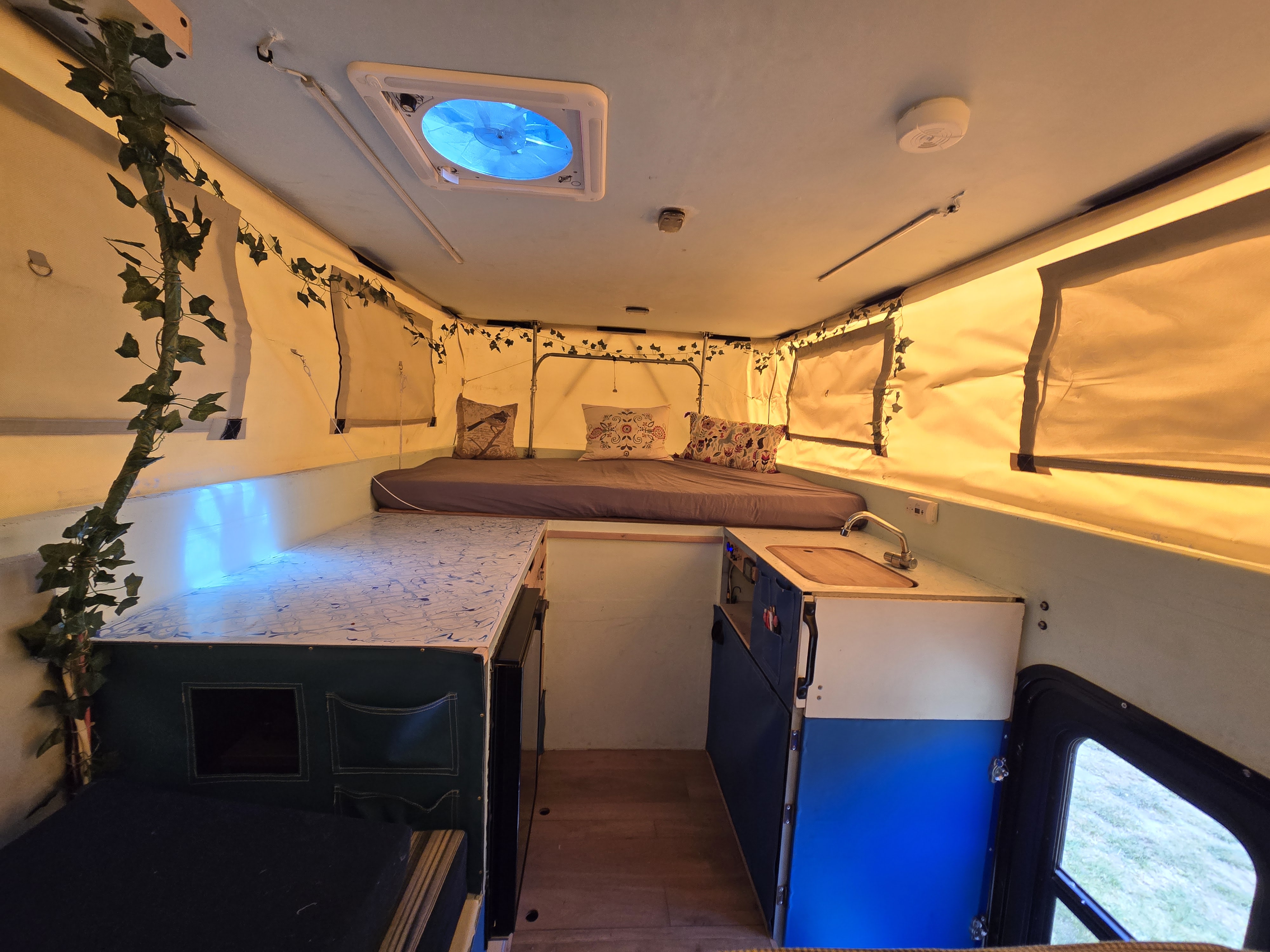 Cozy RV rental pop-up camper interior. Features a bed, kitchen sink, counter, blue fan light, and charming ivy decor.. Toyota Tundra 2005