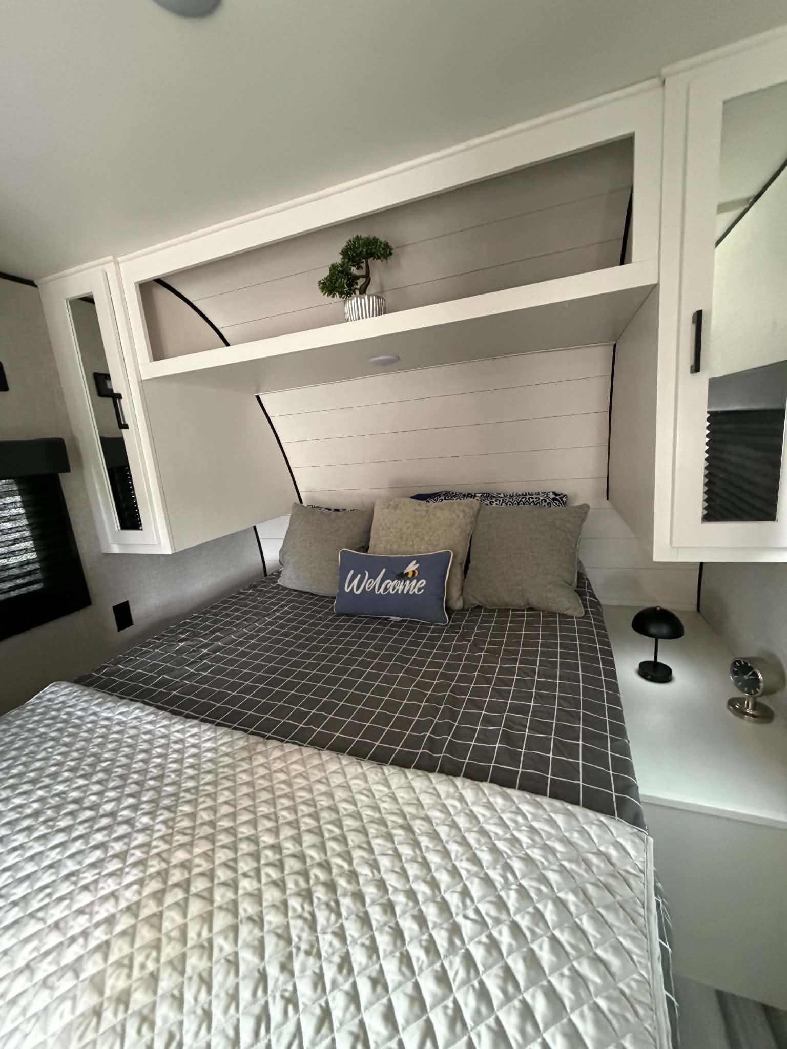 Cozy RV rental bedroom with a comfy bed, "Welcome" pillow, white shiplap headboard, and overhead storage.. Jayco Go play 2024