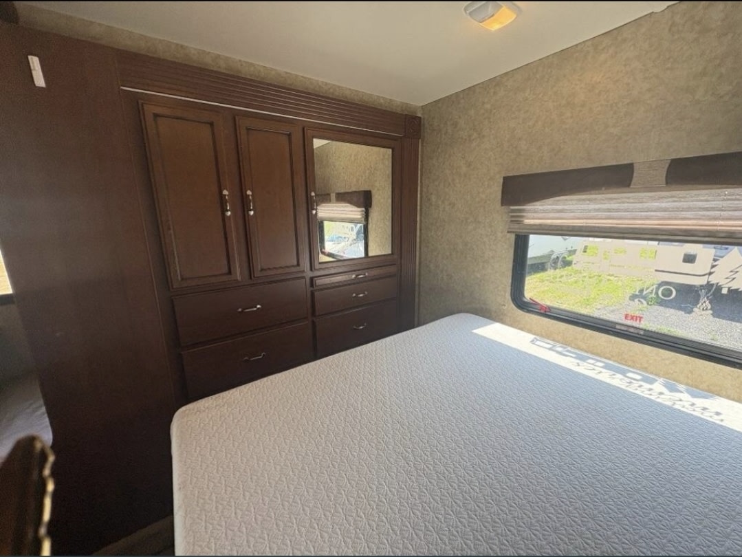 RV rental bedroom showing a white bed, dark wood wardrobe with mirror, and a window overlooking an outdoor scene.. Storm Storm Motorhome 2012
