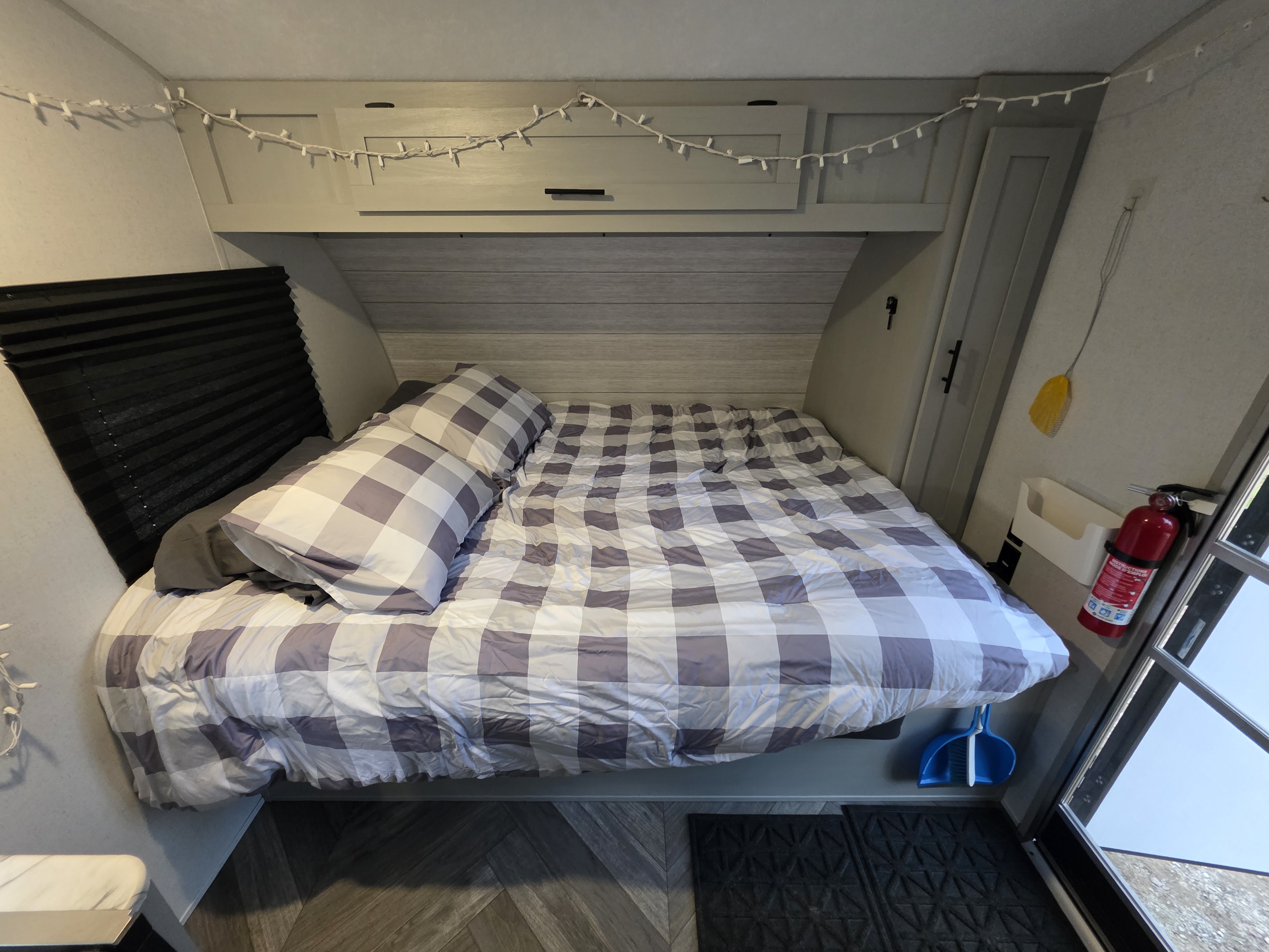 Cozy RV rental bedroom with plaid bedding, overhead storage, string lights, and a fire extinguisher near the exit.. Forest River Wildwood FSX Platinum 2021