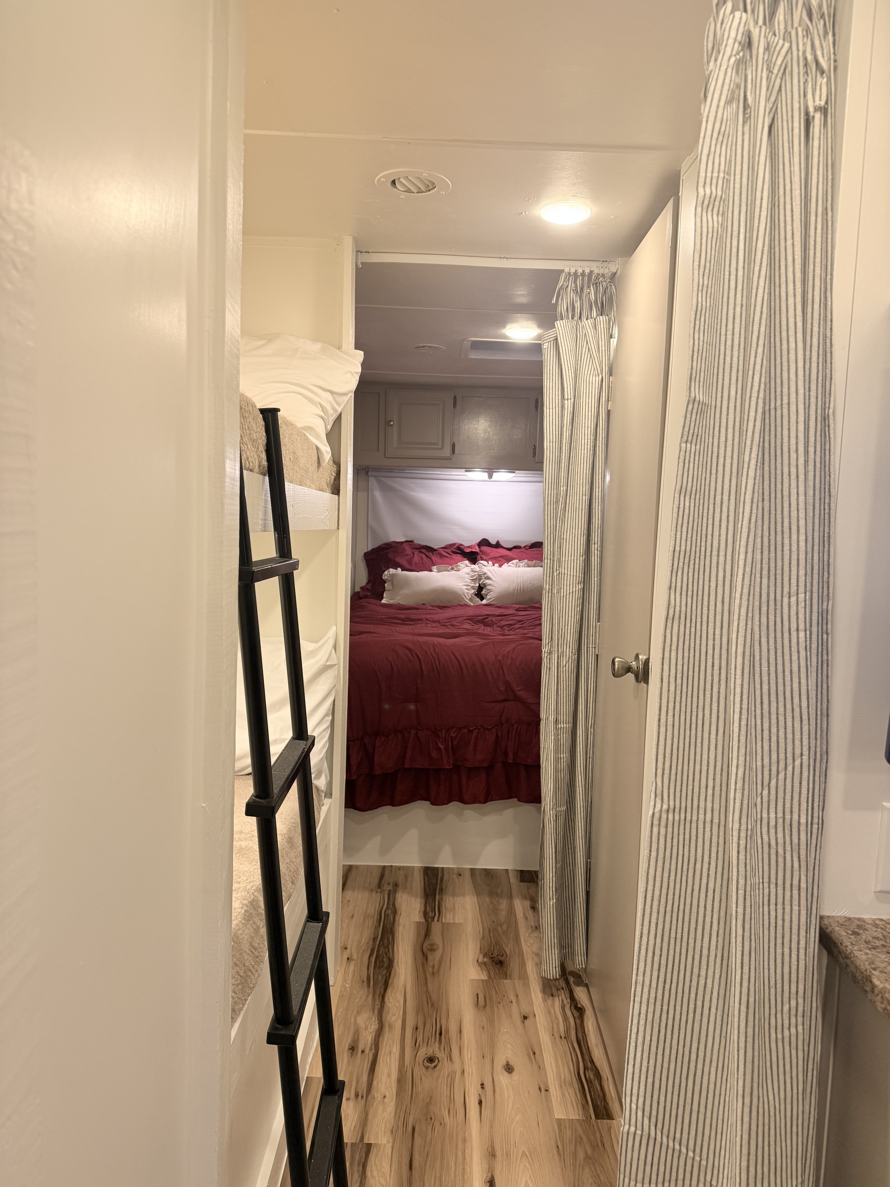 **rv rental** interior: Hallway view with bunk beds & ladder, leading to a bedroom with red bedding. Striped curtain and wood floor.. Gulf Stream Stream Lite 2008