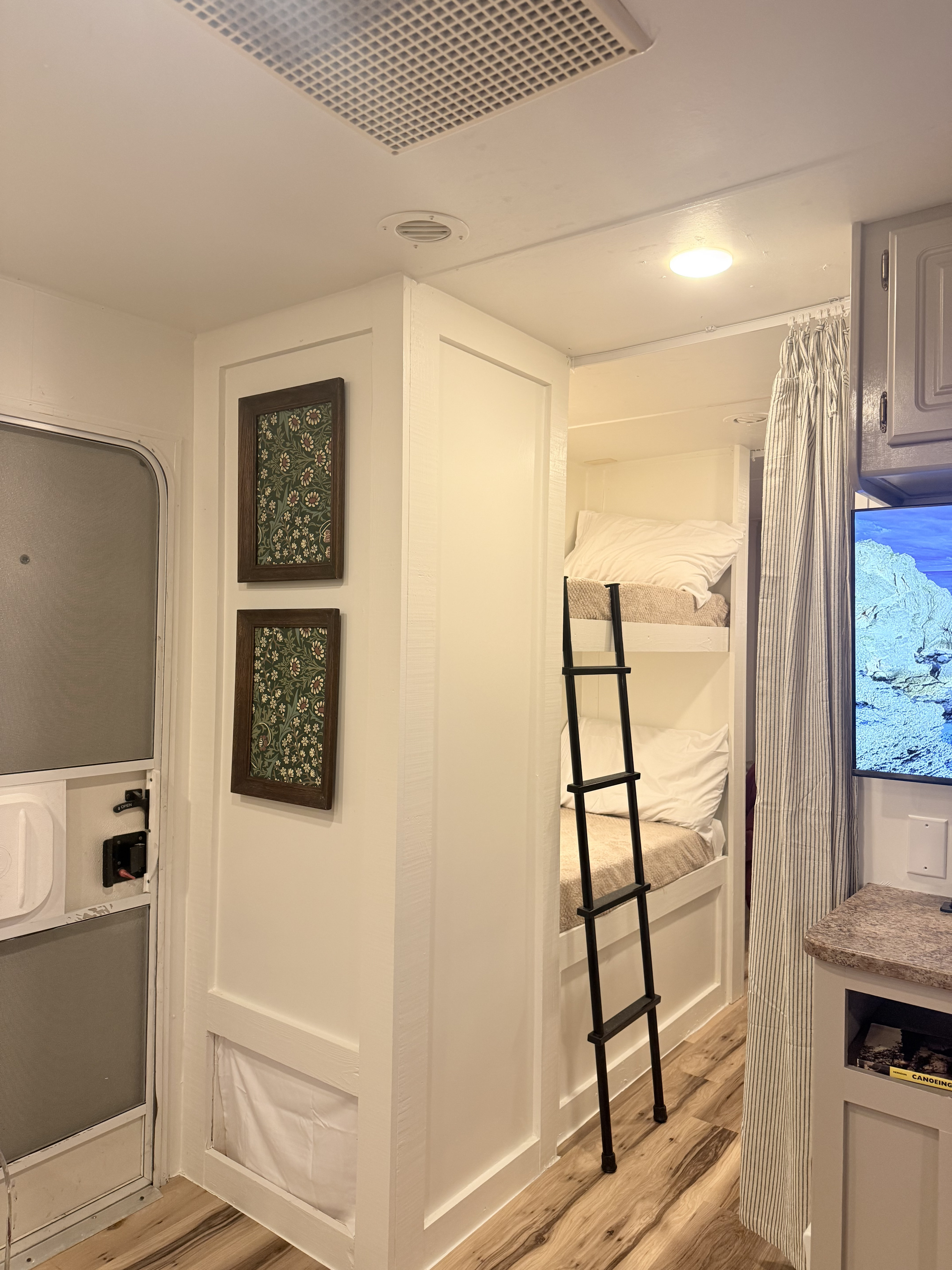 Cozy RV rental interior with white bunk beds, a black ladder, and framed floral art. A bright and functional camper space.. Gulf Stream Stream Lite 2008