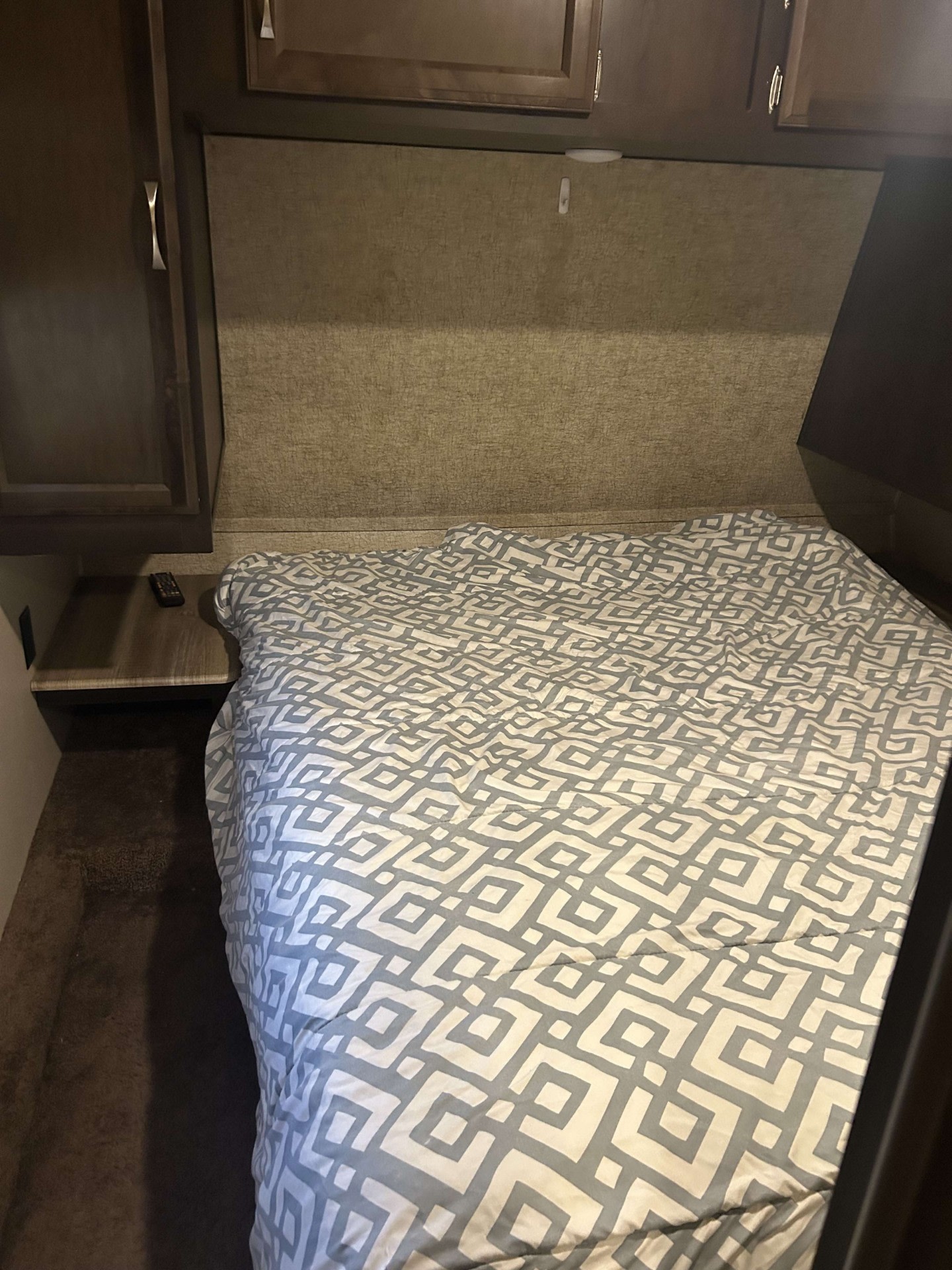 Inside an RV rental, a compact bedroom with a bed featuring a gray and white geometric comforter, built-in storage, and carpeted floor.. Heartland RVs Prowler Toy Hauler 2017