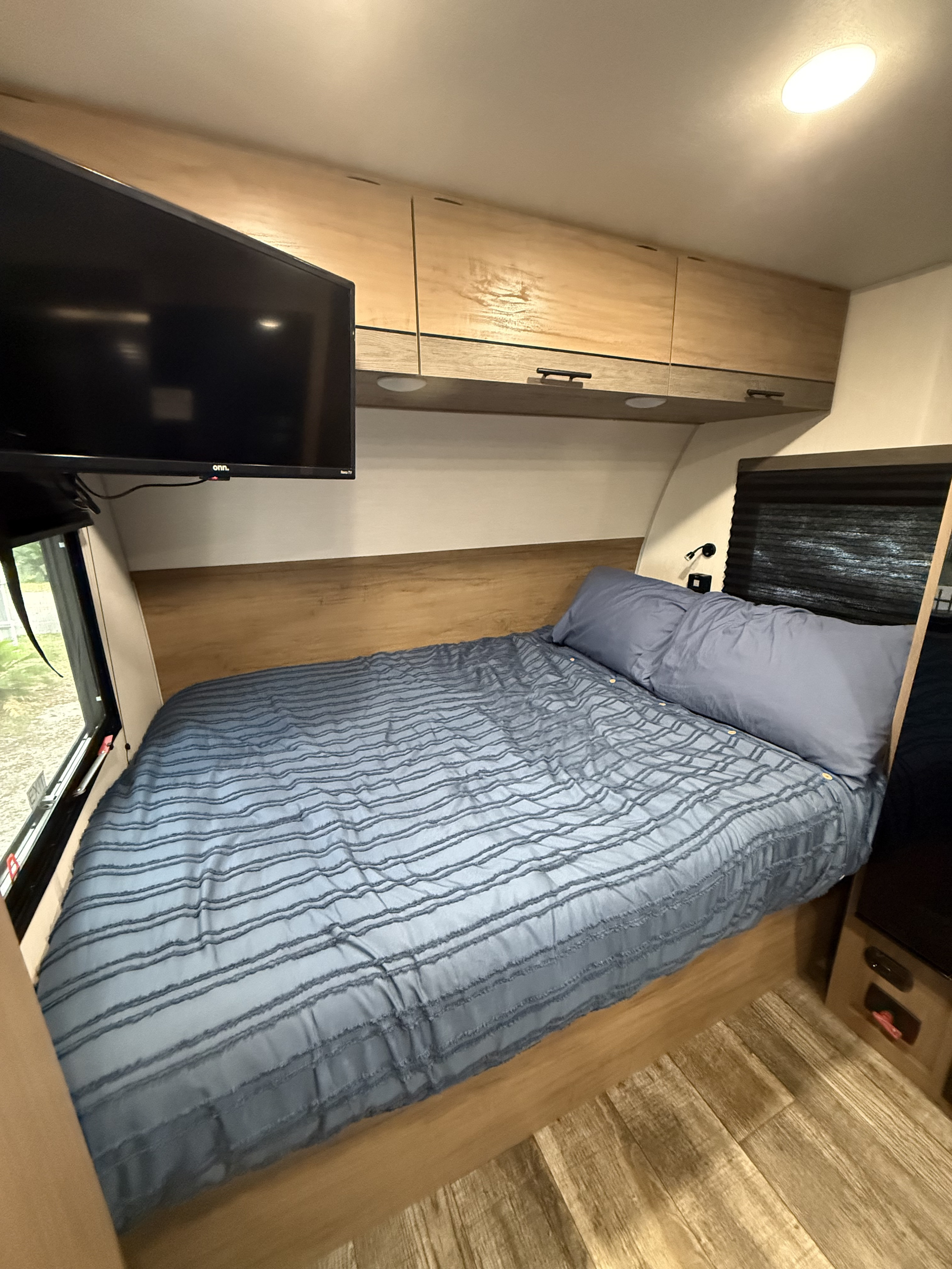 Cozy RV rental bedroom featuring a comfy blue bed, wall-mounted TV, and handy overhead cabinets. Perfect for on-the-road stays.. Forest River Campsite Reserve LS17 2025