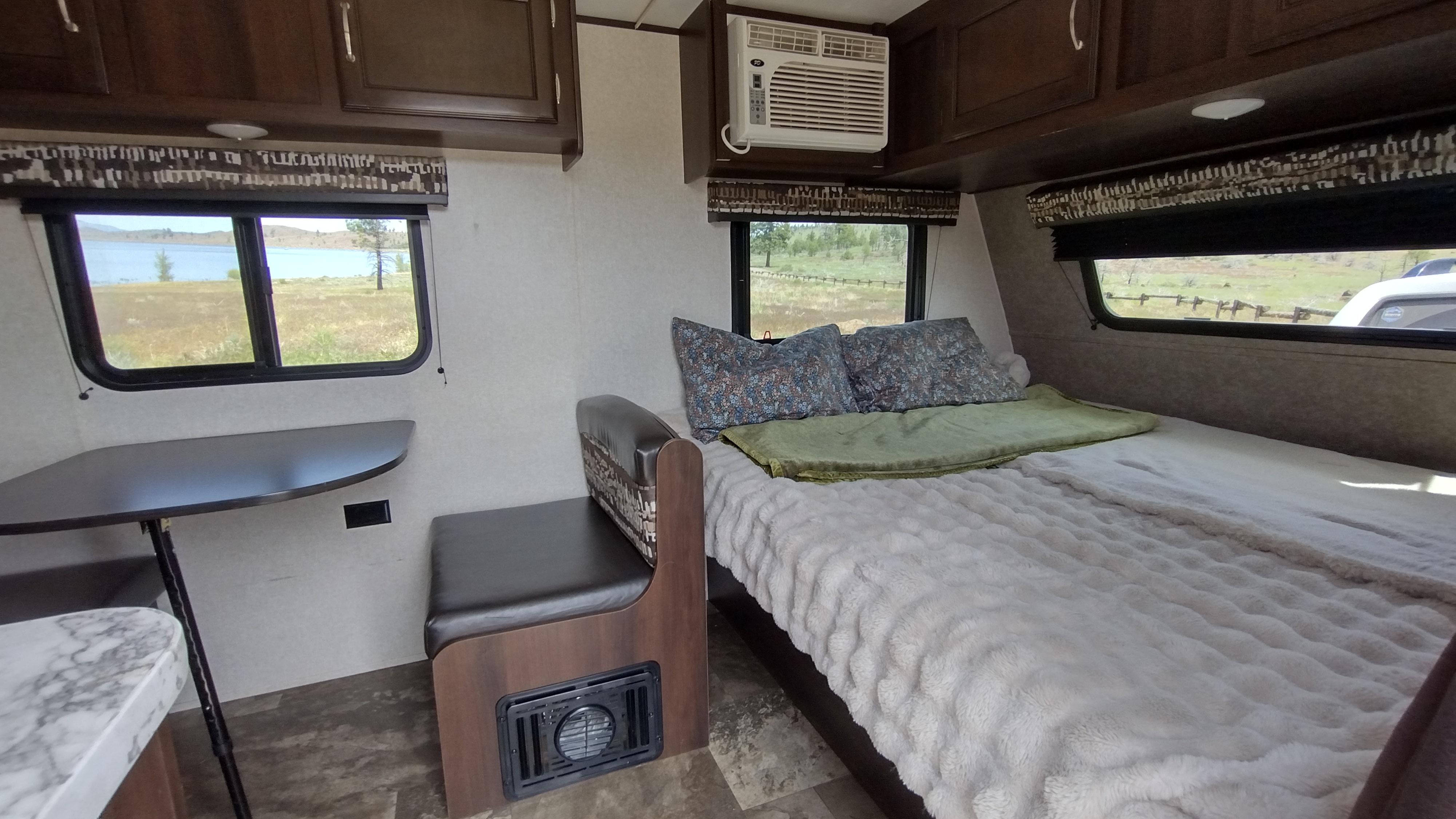 Cozy RV rental interior with a bed, dinette, and AC unit, offering a scenic lake view from the windows.. Jayco Jay Flight SLX 2018