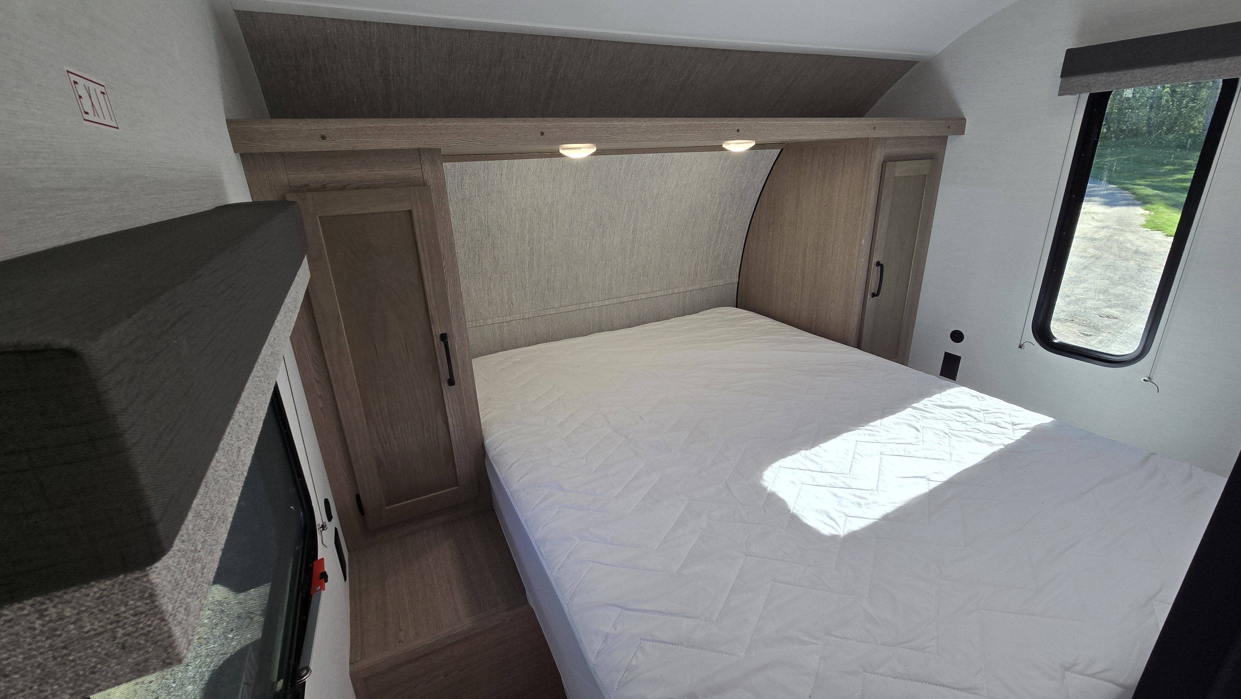 A bright RV rental bedroom showing a bed with white bedding, flanking storage cabinets, reading lights, and a scenic window view.. Gulf Stream 268BH 2026