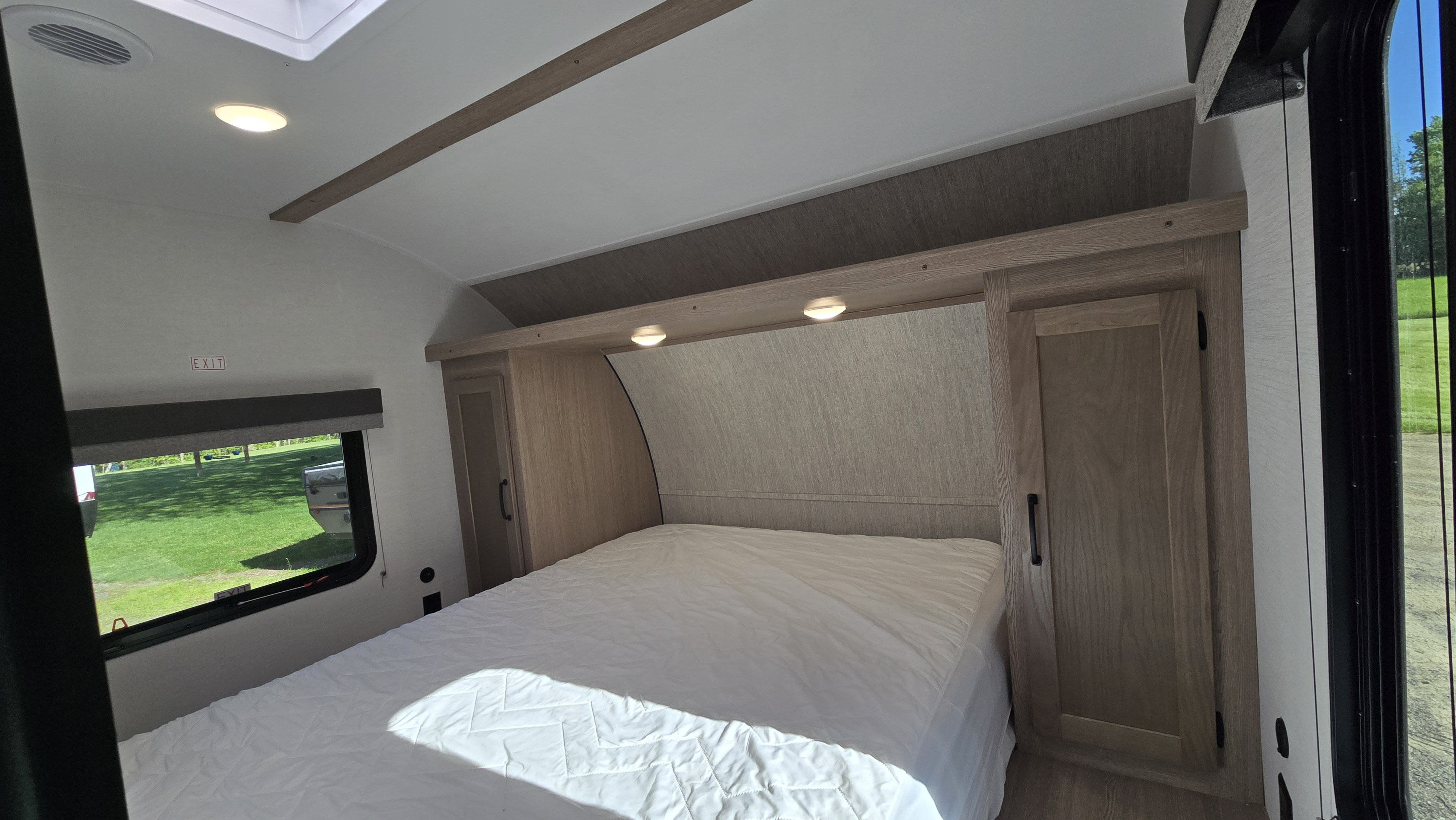 RV rental bedroom interior with a white bed, window showing greenery, built-in cabinets, and overhead lighting/skylight.. Gulf Stream 268BH 2026