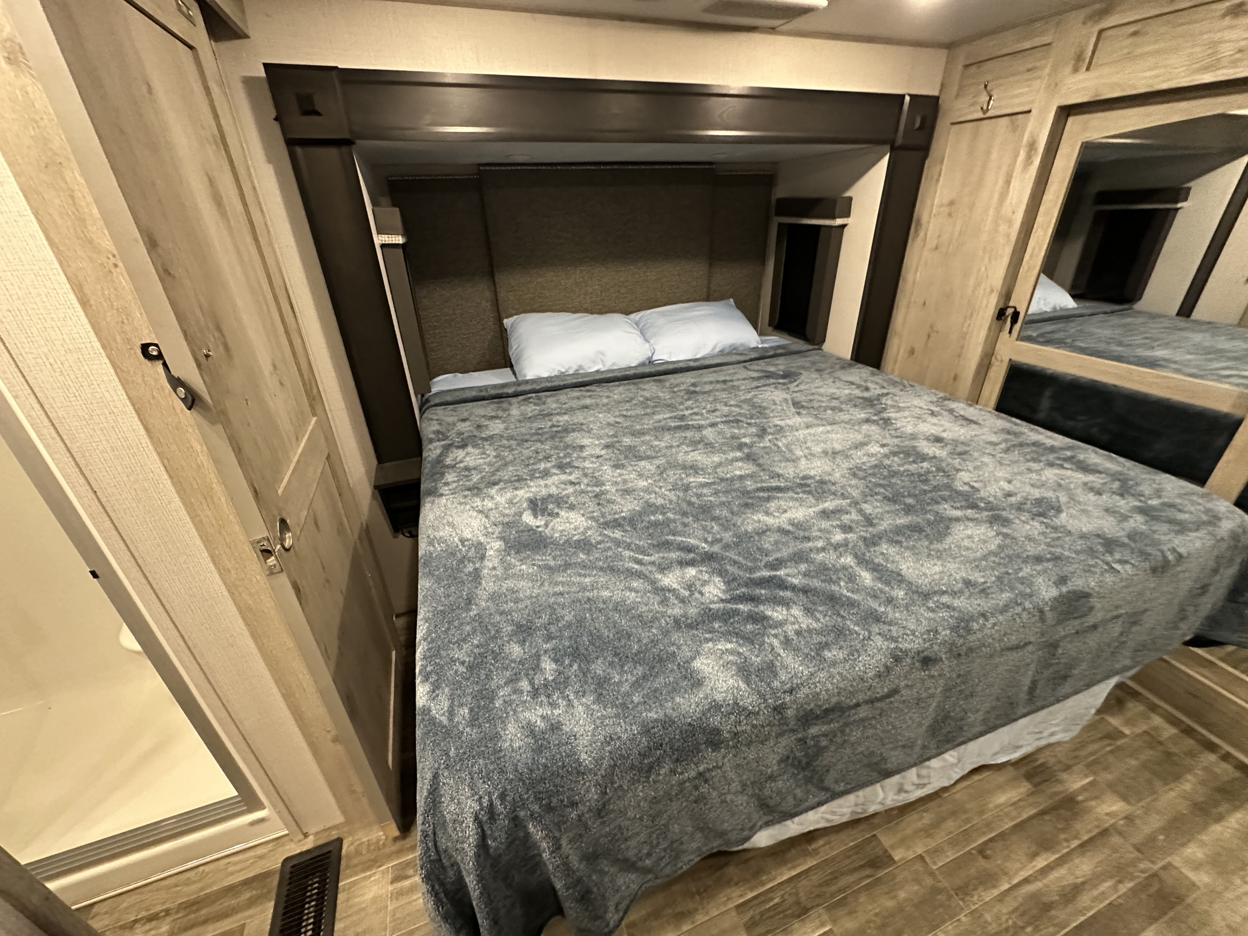 Compact RV rental bedroom featuring a comfortable bed, integrated storage, and modern wood-look flooring. Ideal for road trips.. Keystone RV Avalanche 2021