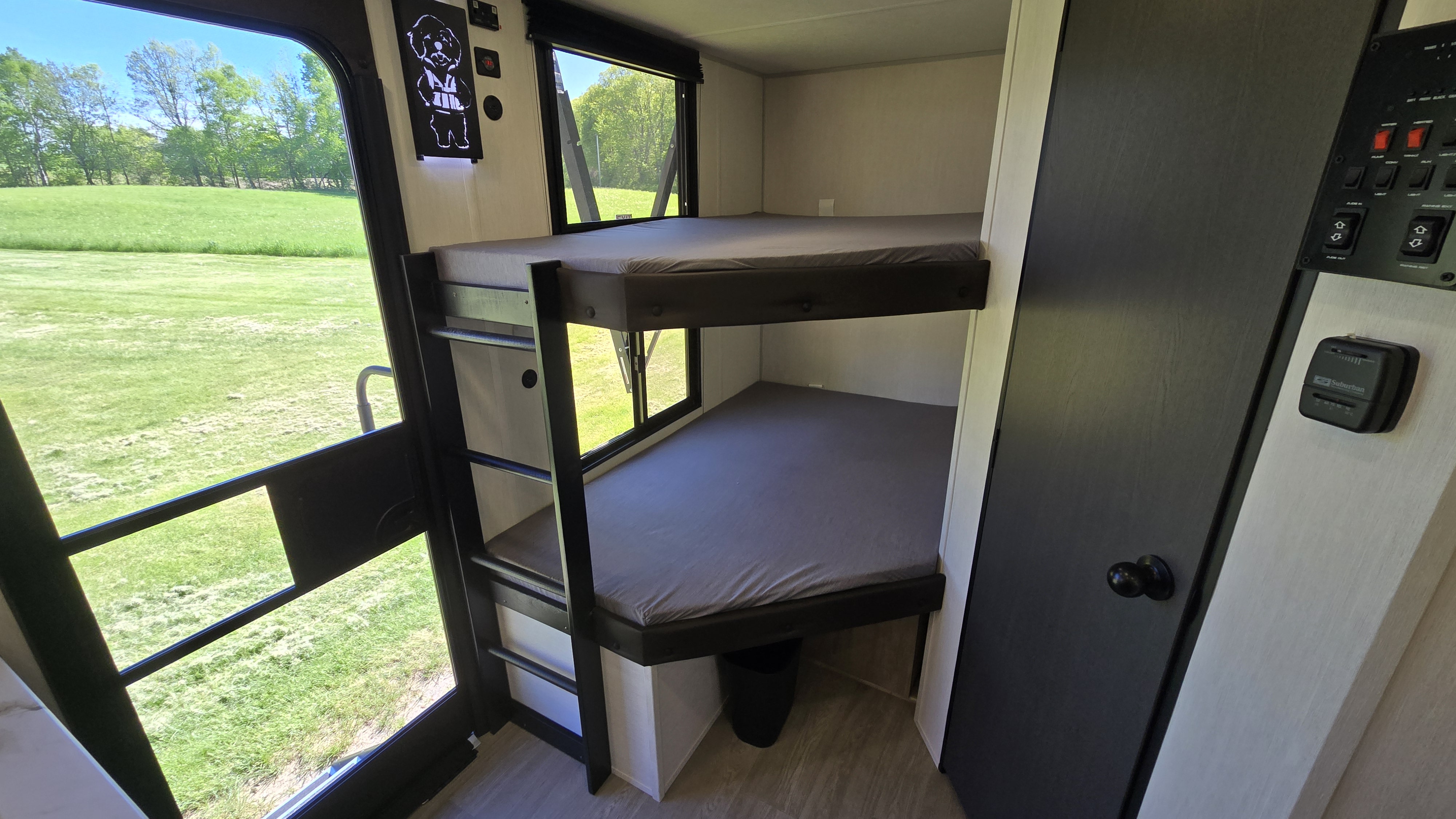 Cozy RV rental featuring bunk beds, large windows with a scenic green field view, and interior controls.. Forest River Campsite Reserve 2026