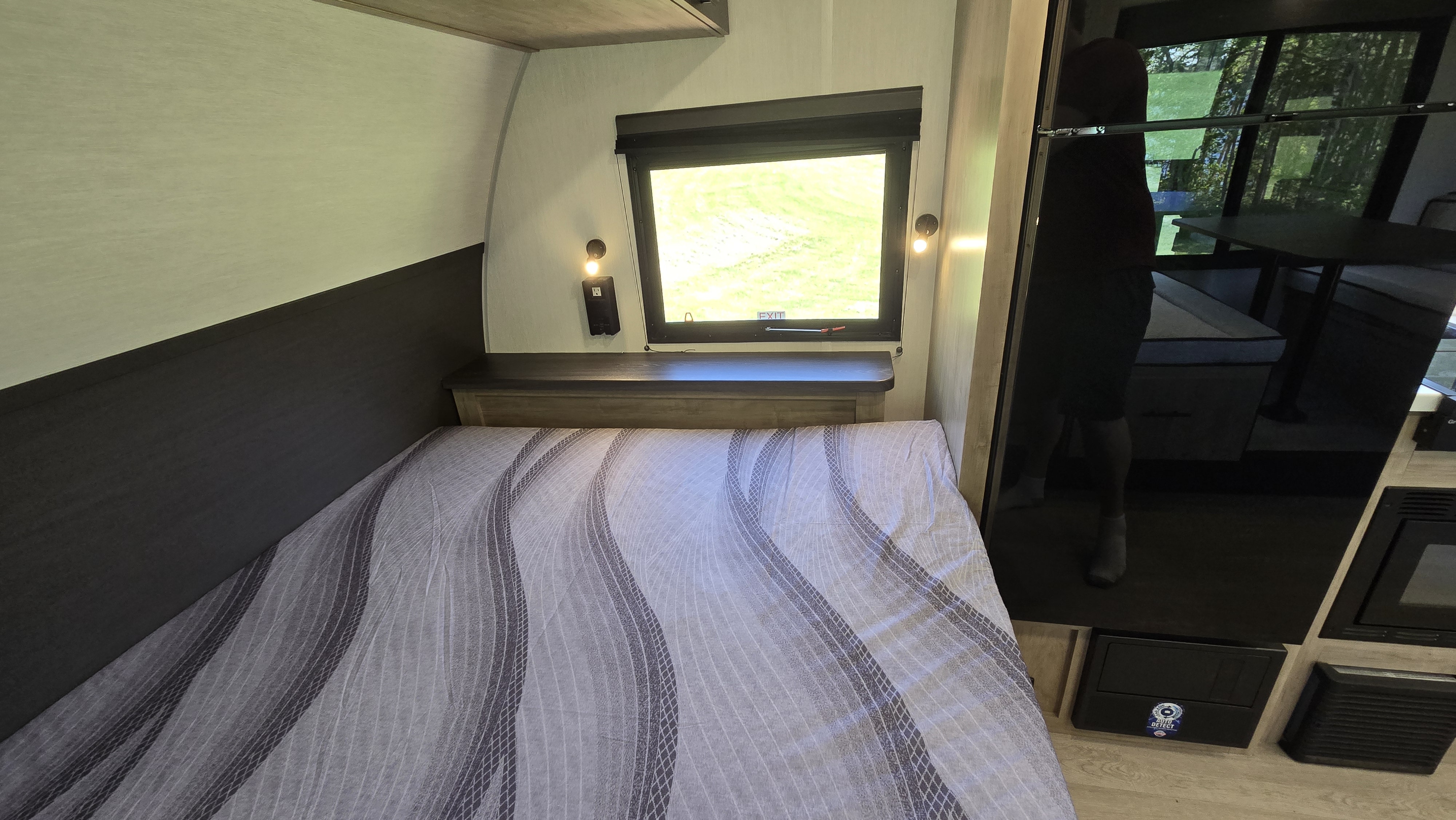 RV rental interior: cozy bedroom with a striped bed, window overlooking greenery, and built-in amenities for travel comfort.. Forest River Campsite Reserve 2026