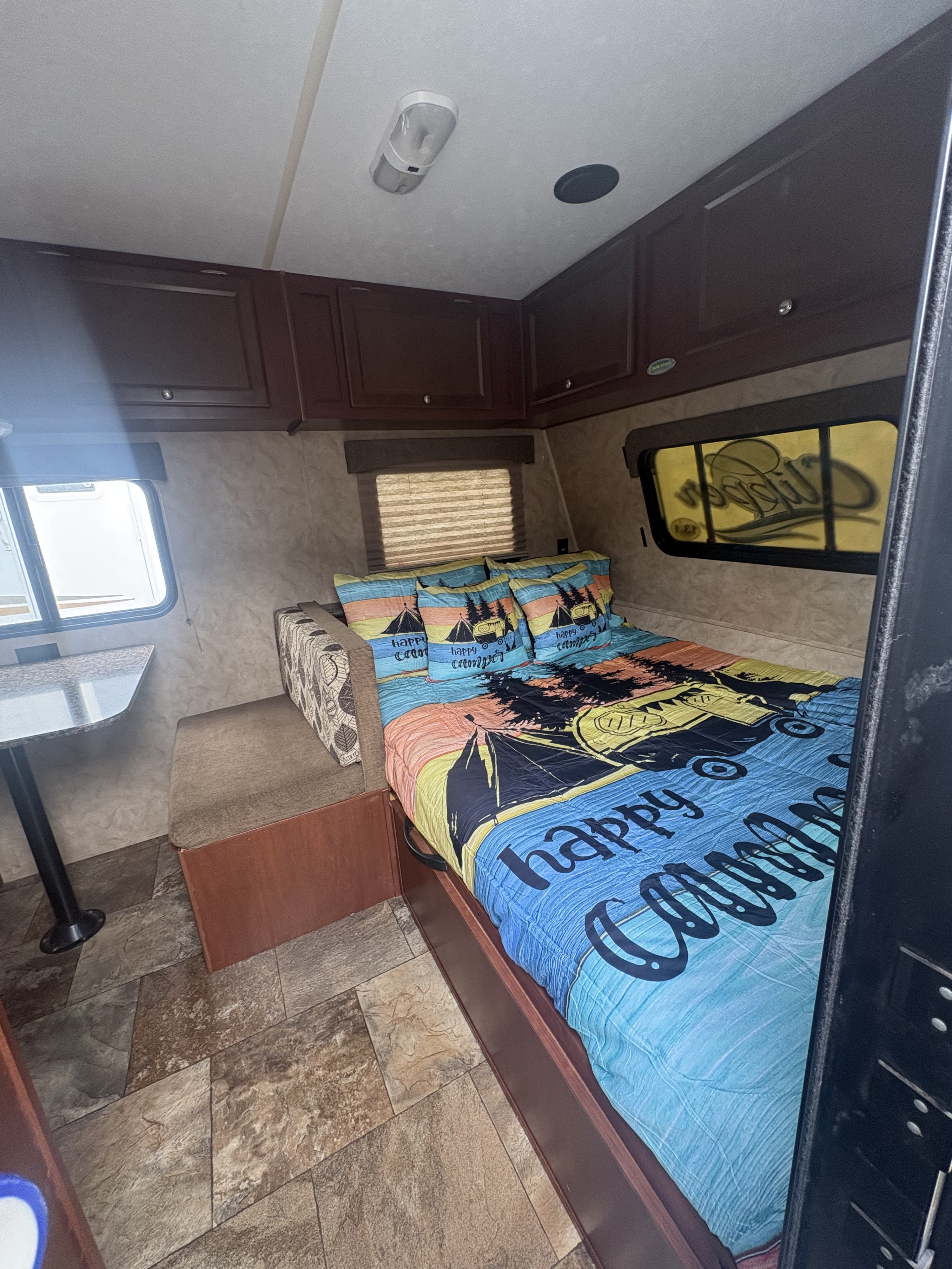RV rental interior: cozy bedroom featuring "happy camper" bedding, storage cabinets, and a dining nook with a window.. Coachmen Clipper 17BH 2015
