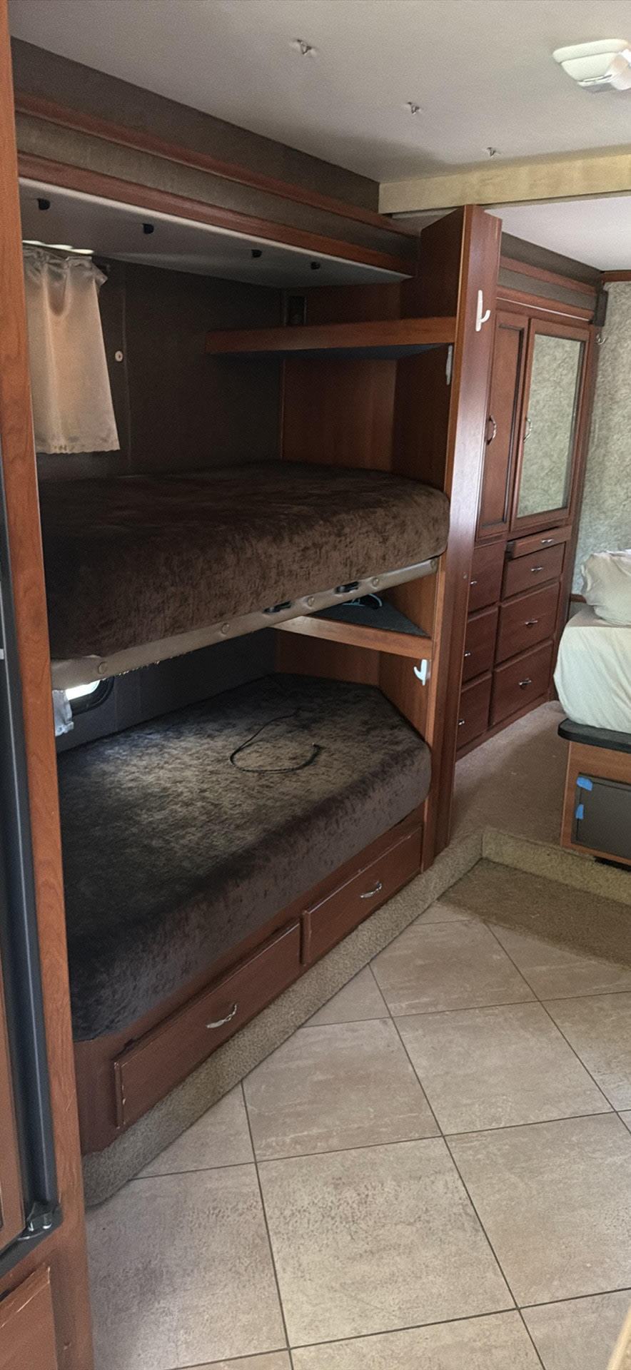 RV rental interior featuring comfortable bunk beds with drawers, wooden cabinetry, and a main bed in the background.. Fleetwood 31C 2015