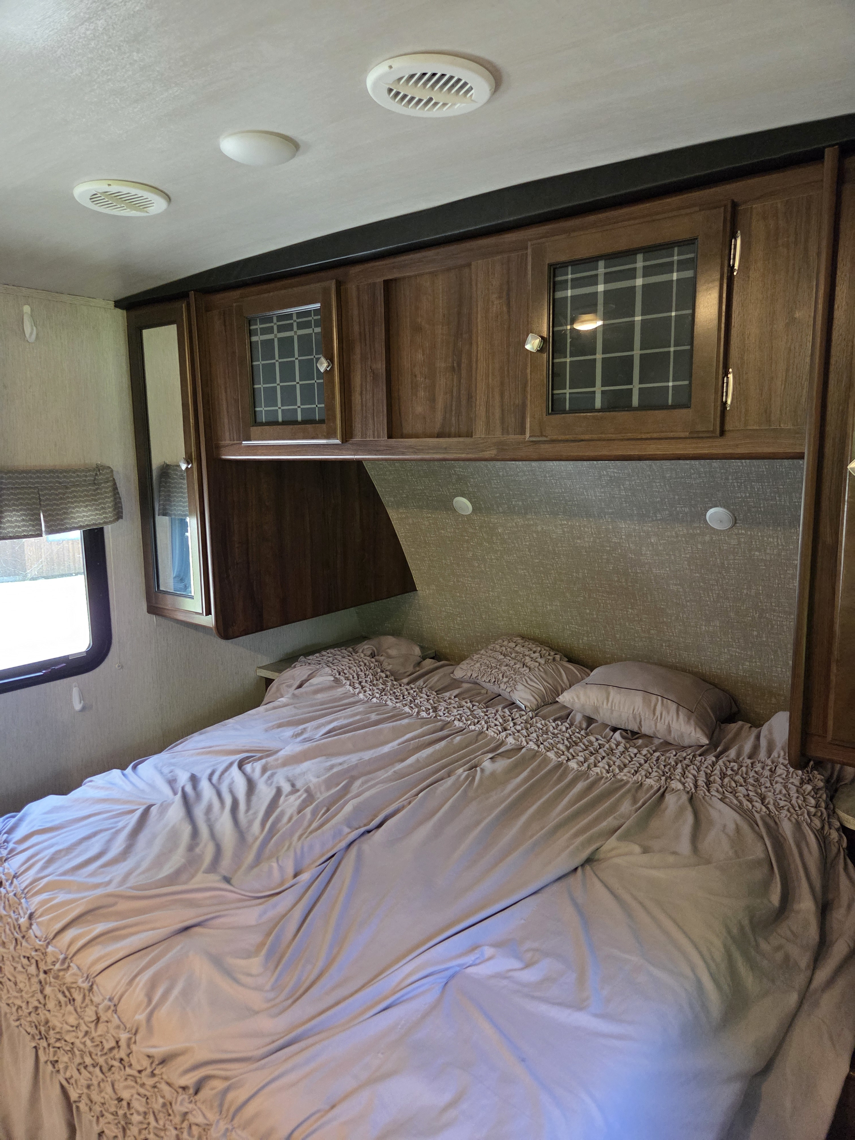 Relax in this comfortable RV rental bedroom, featuring a large bed, built-in overhead cabinets, and a side window.. Heartland RVs Wilderness 2018