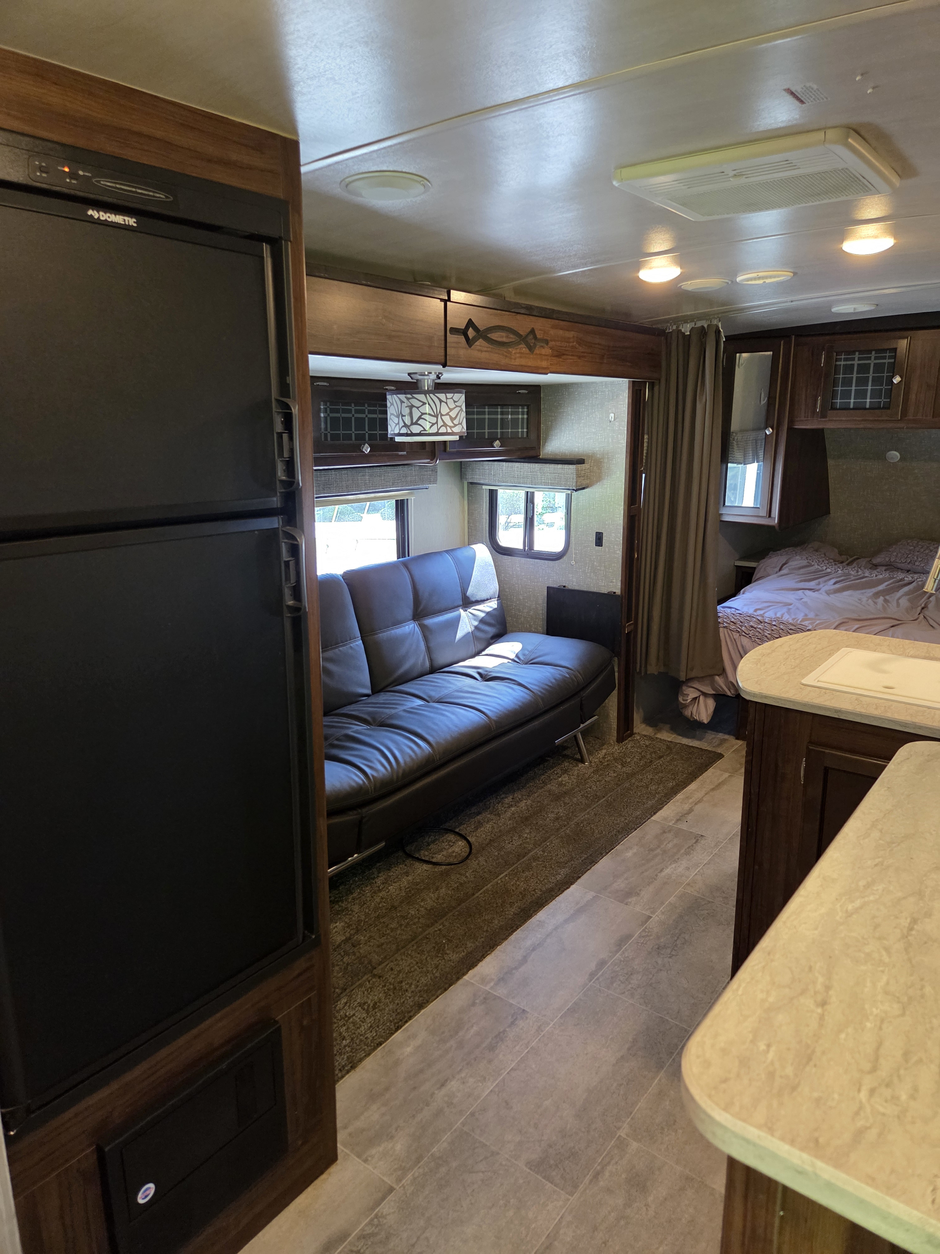 Cozy RV rental interior featuring a Dometic fridge, black sofa, bed, and kitchenette. Perfect for your next adventure!. Heartland RVs Wilderness 2018