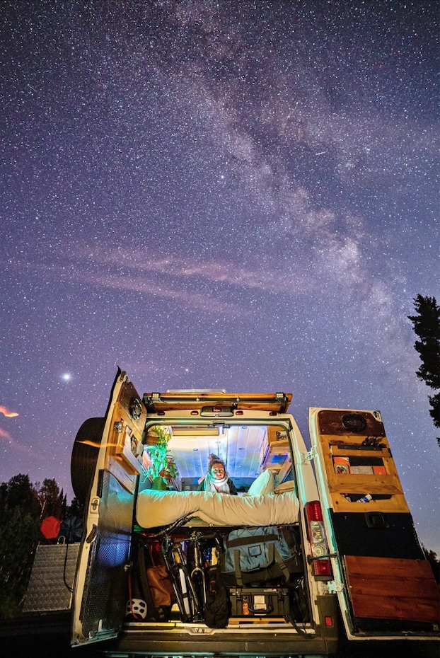 Stargazing under the Milky Way from a cozy RV rental camper van. The illuminated interior shows a person relaxing.. RAM ProMaster 2500 2016