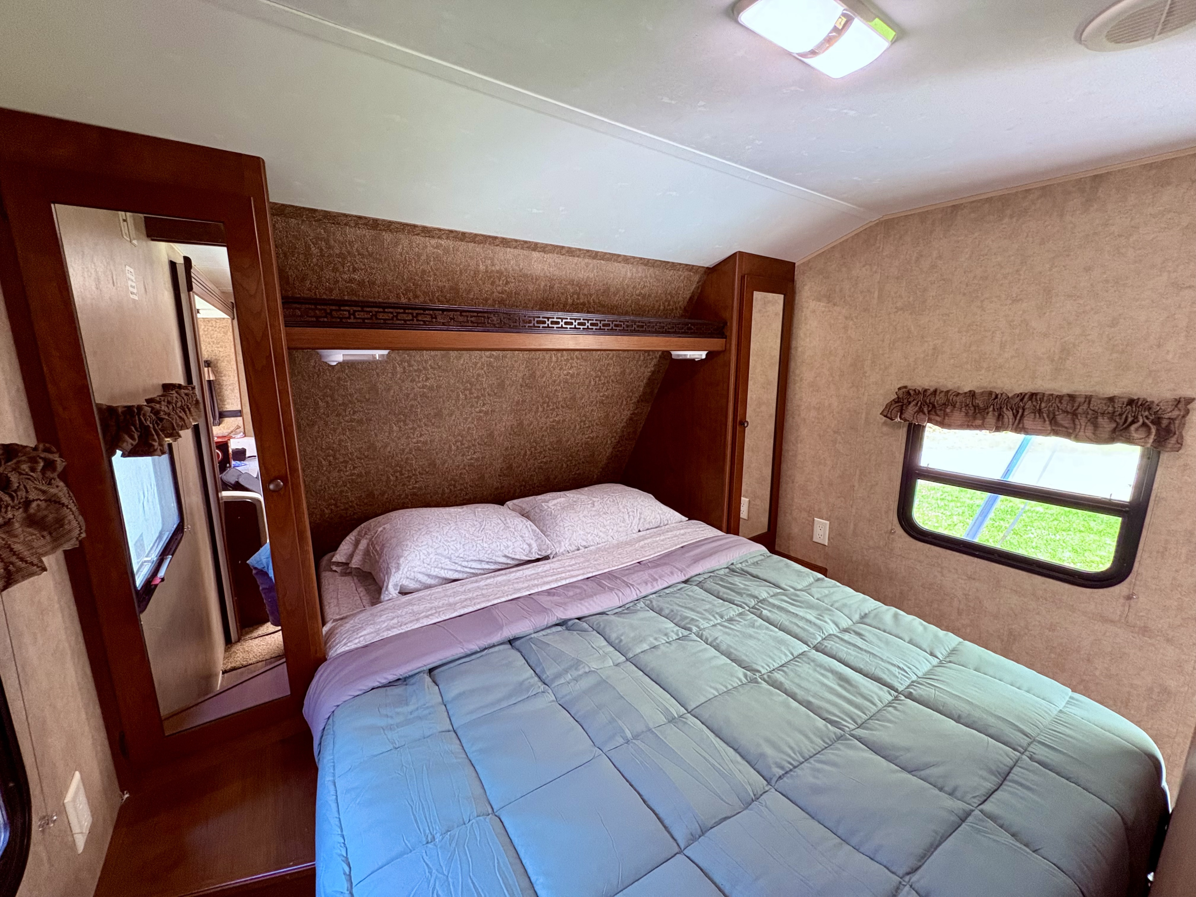 Cozy RV rental bedroom featuring a comfortable bed, overhead storage, and a window with green views. Perfect interior for travel.. Dutchmen Aspen Trail 2013