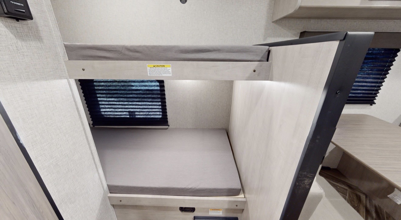 This rv rental features compact bunk beds, providing comfortable sleeping space. Two mattresses are visible, with window blinds and interior lighting.. Crossroads RV Zinger 2025