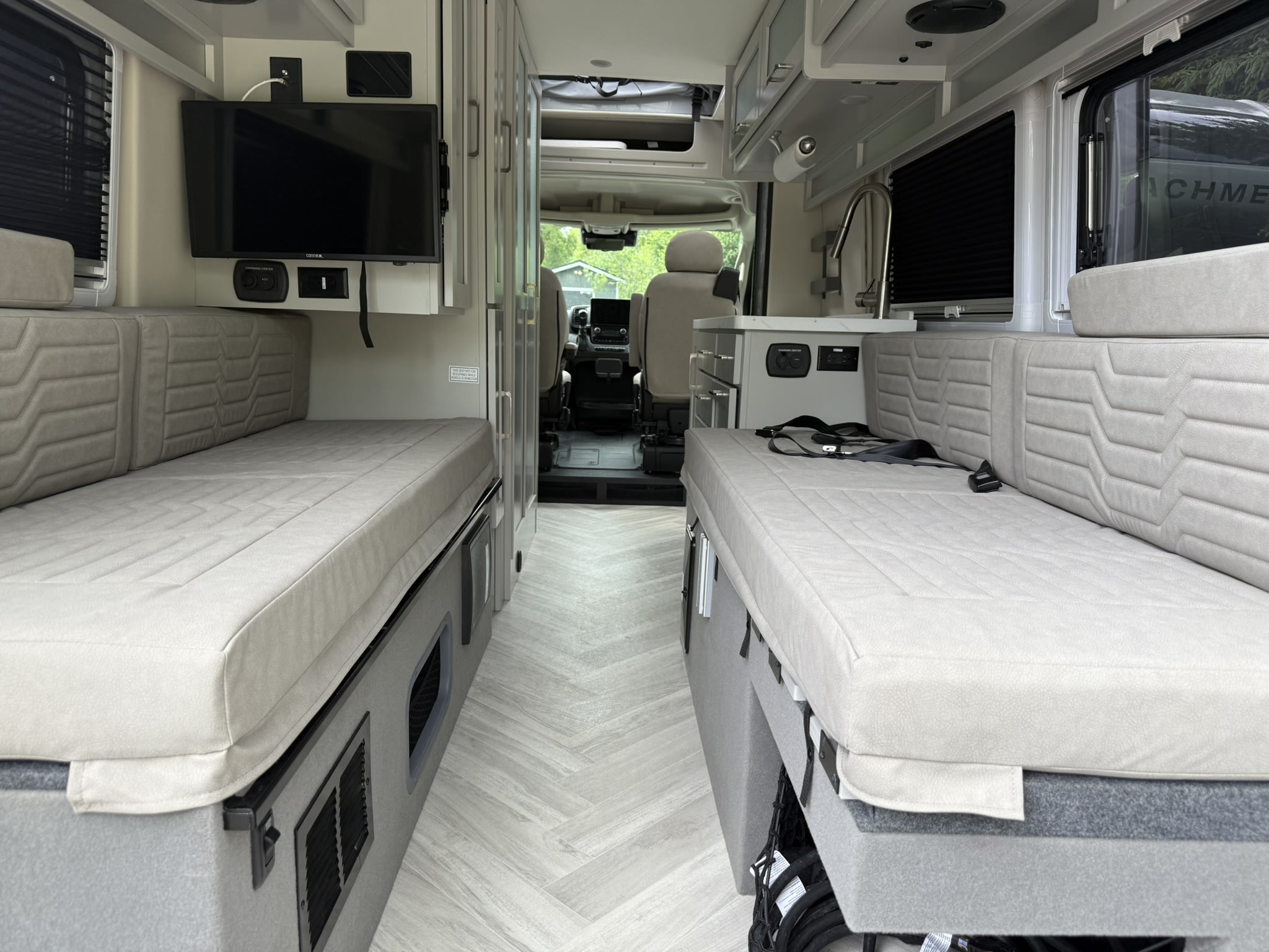 Interior of an rv rental showing two long bench seats/beds, a TV, kitchen area, and front cabin view with light flooring.. Coachmen Nova 2024