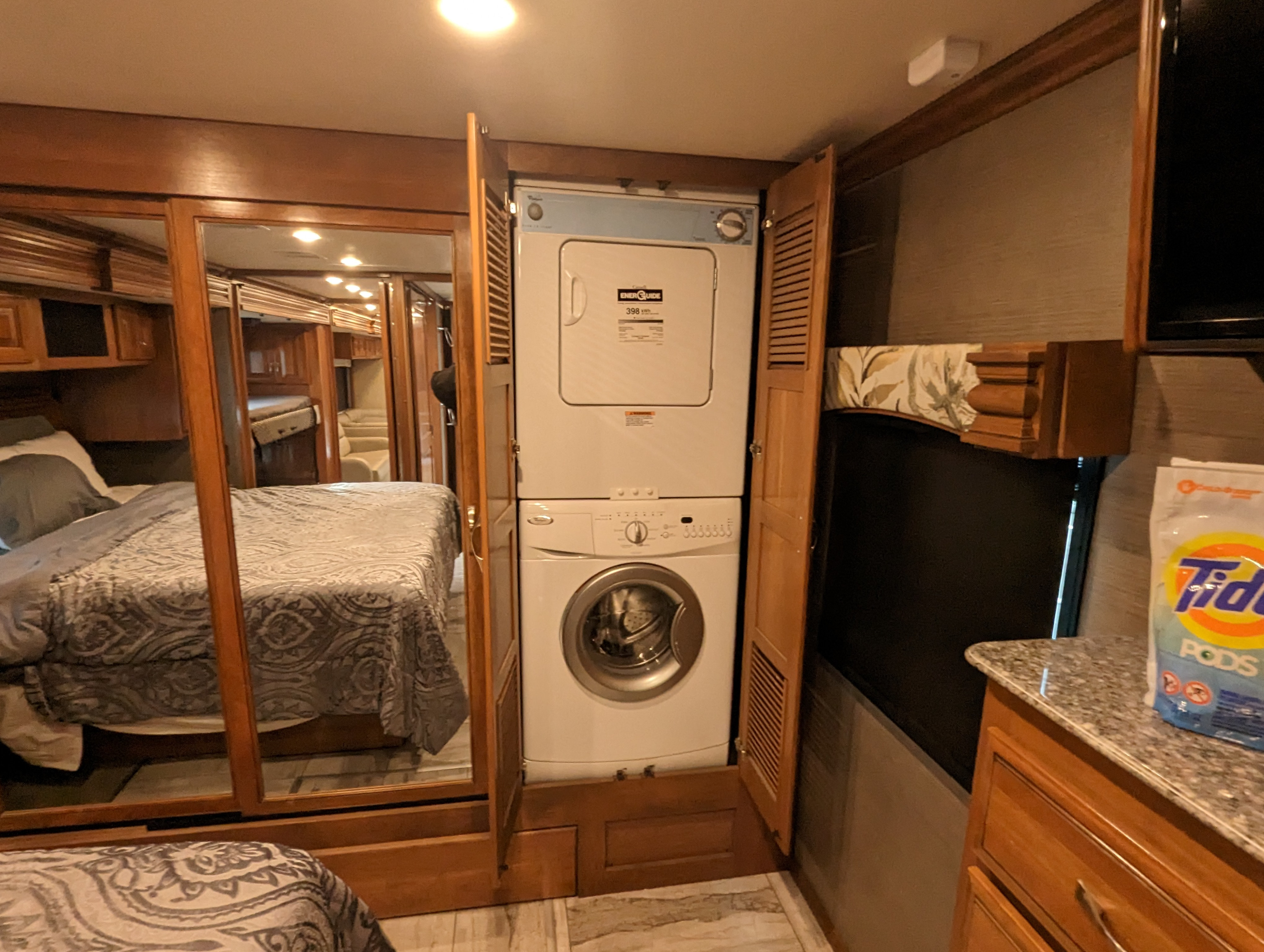 RV rental: Compact motorhome bedroom with mirrored closet, stacked washer/dryer, and laundry supplies.. Fleetwood Discovery 2017