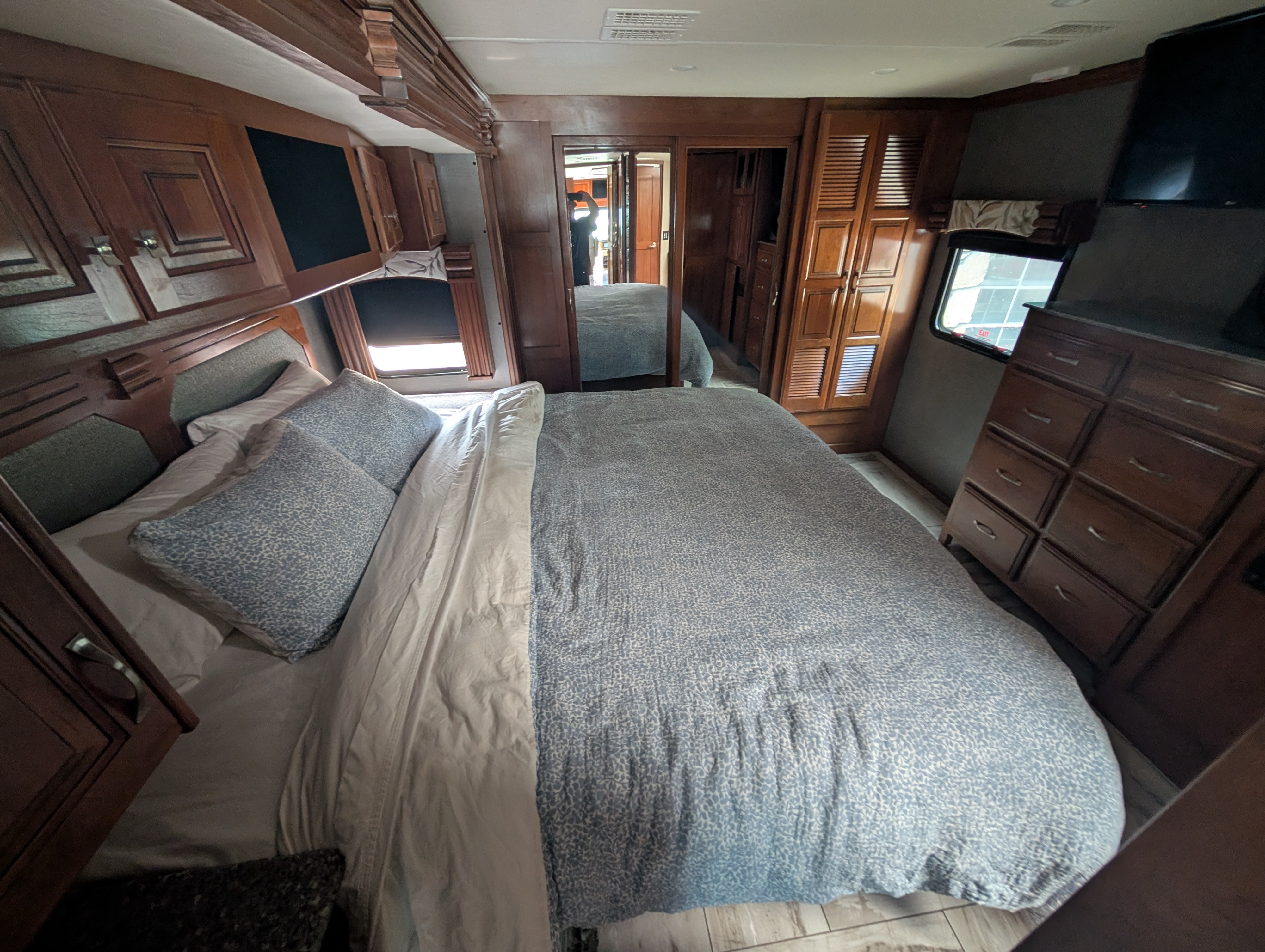 Spacious RV rental bedroom with a large bed, blue patterned bedding, wood cabinets, dresser, and a wall-mounted TV.. Fleetwood Discovery 2017