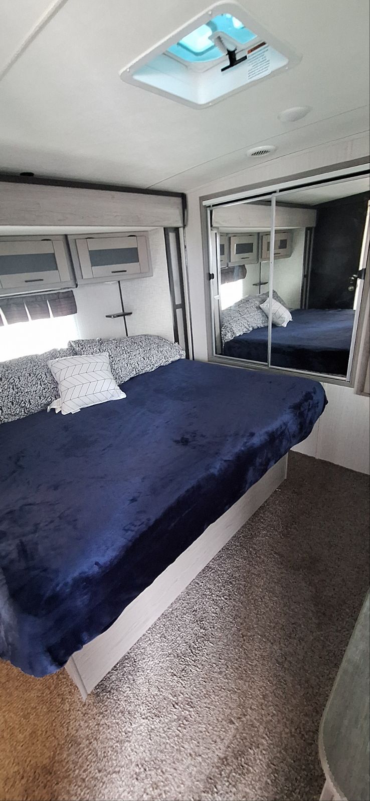 Cozy RV rental bedroom with a large bed, navy blanket, skylight, overhead cabinets, and mirrored closet.. Heartland RVs Mallard 2020