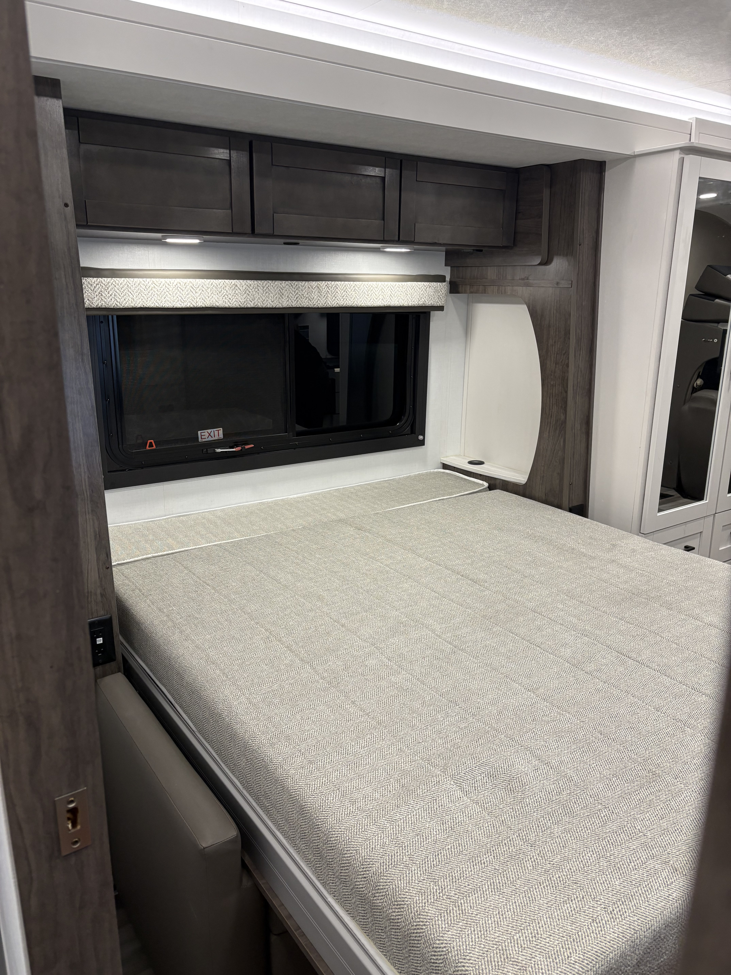 Experience comfort in this RV rental bedroom with a light herringbone bed, dark cabinets, and an emergency exit window.. Jayco RedHawks 26M 2026