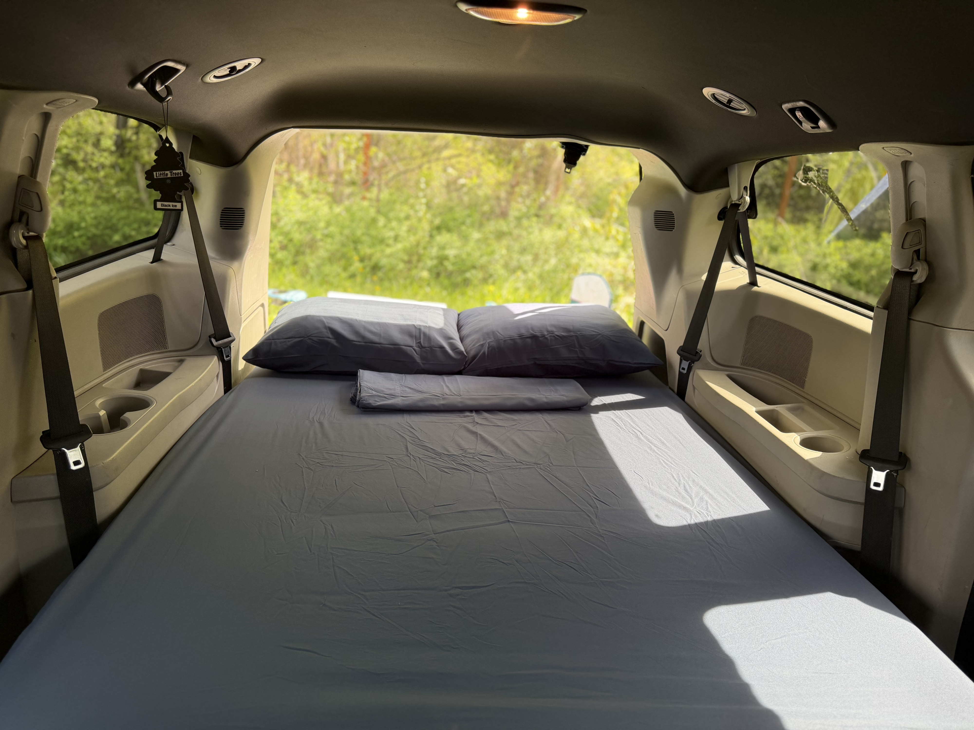 Minivan converted into a sleeping area for an RV rental journey. Features a comfy bed, pillows, and a scenic nature view.. Dodge Grand Caravan 2017