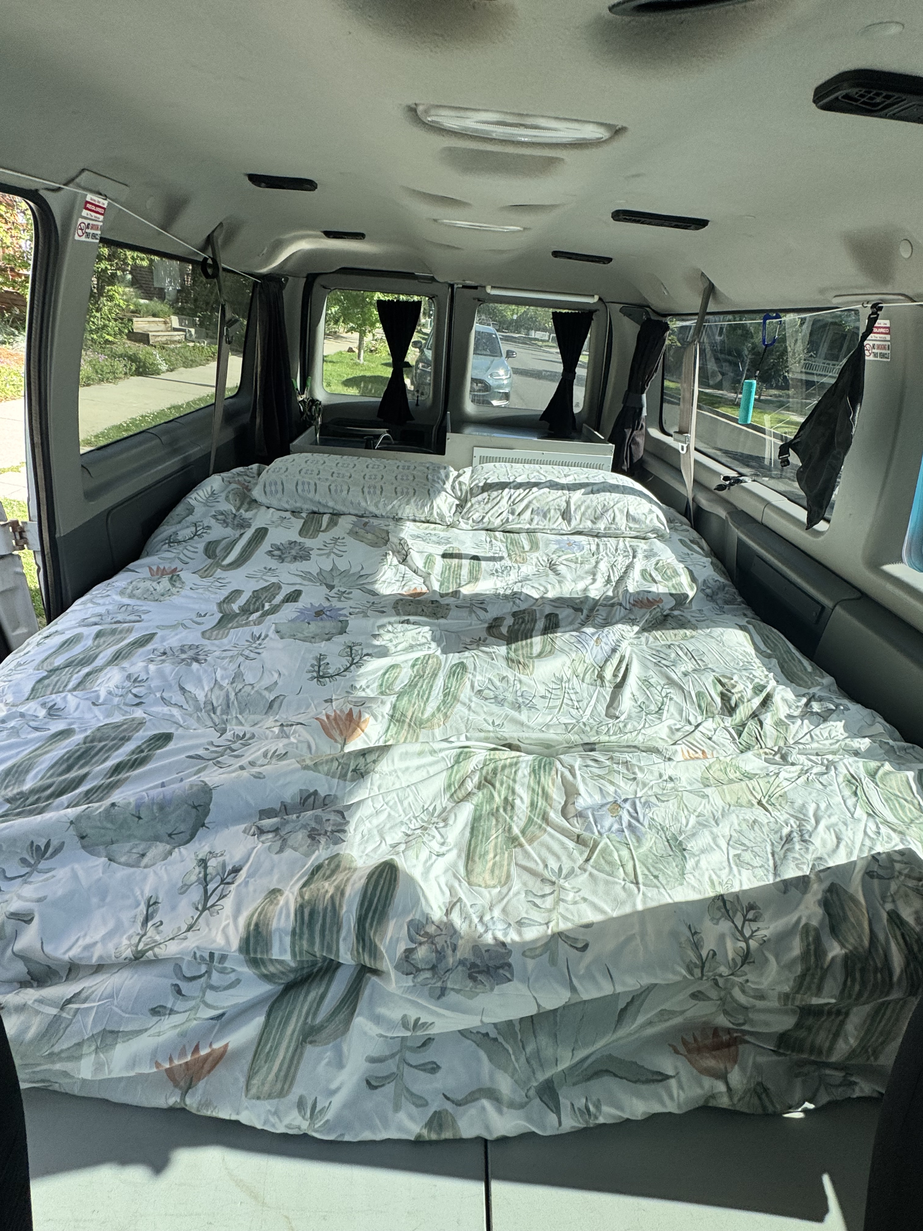 Inside an RV rental: a cozy camper van bed with a unique cactus print comforter, offering a comfortable space for road trips.. Ford Econoline 150 2012