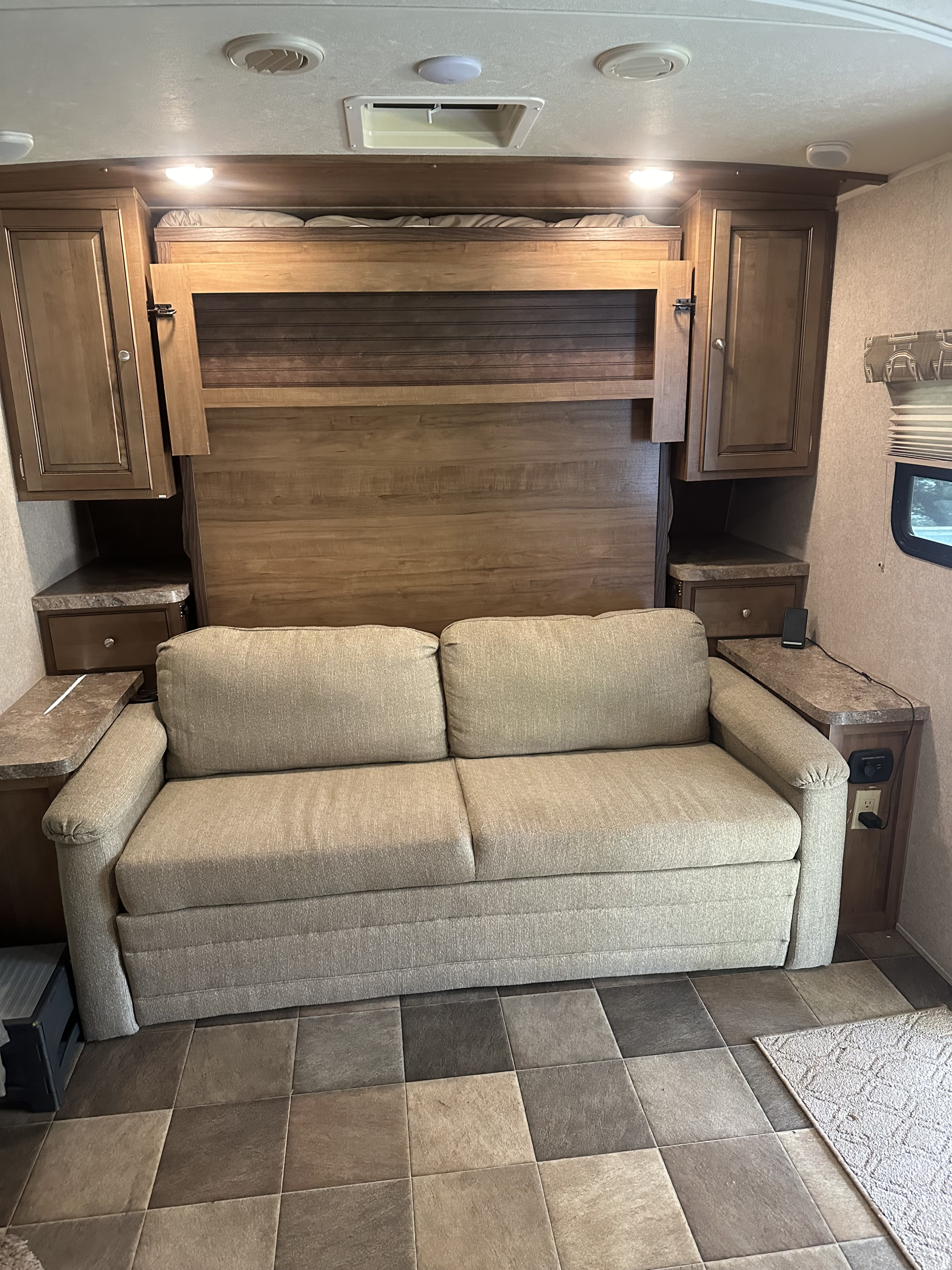 RV rental interior shows a beige sofa bed, murphy bed above, wooden cabinets, and a tiled floor. A functional living space.. Forest River Flagstaff Micro Lite 2017