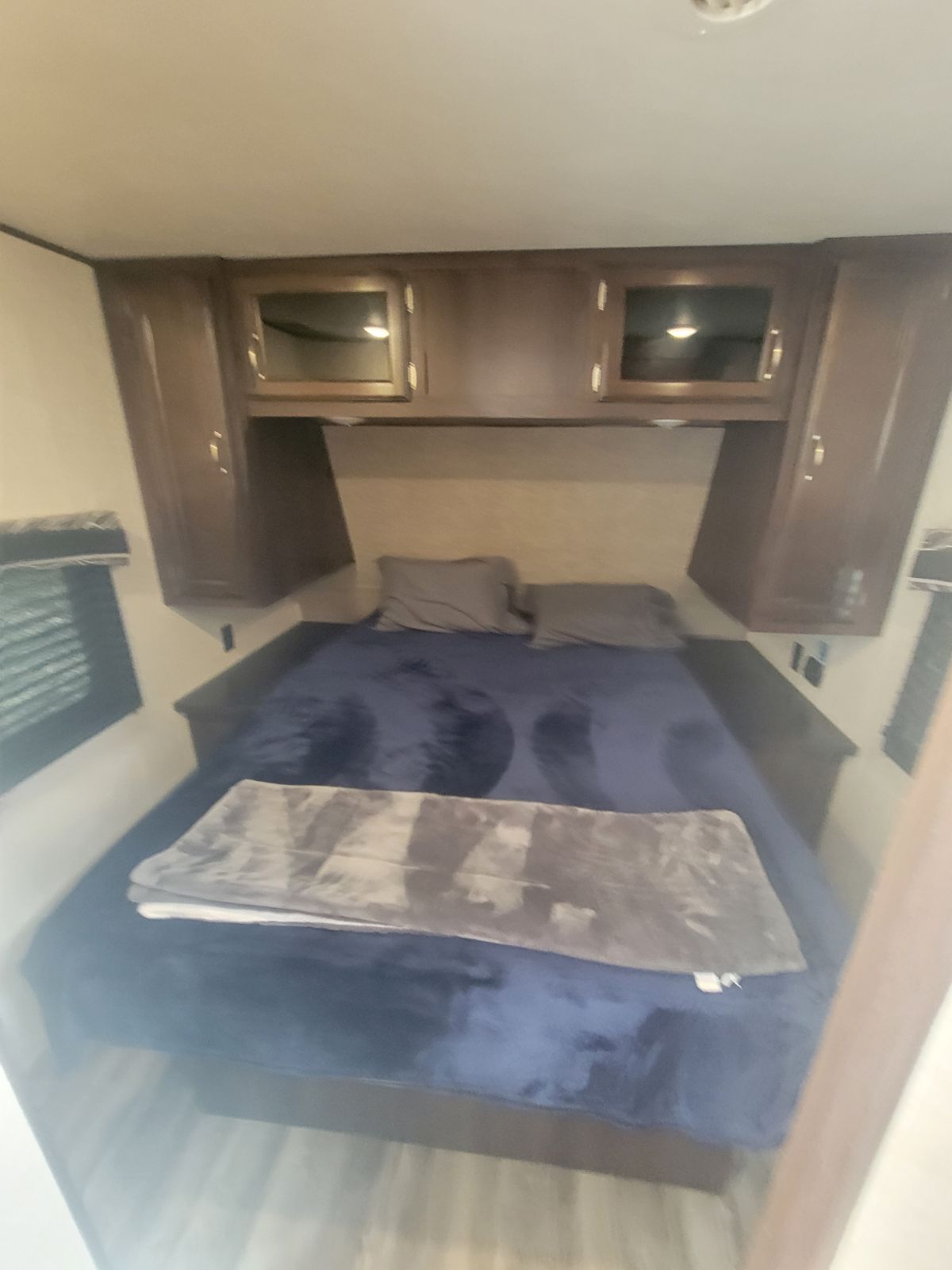Cozy RV rental bedroom with a full bed, blue bedding, gray blanket, and dark wood cabinets above and beside the bed.. Jayco Jay Flight 2019