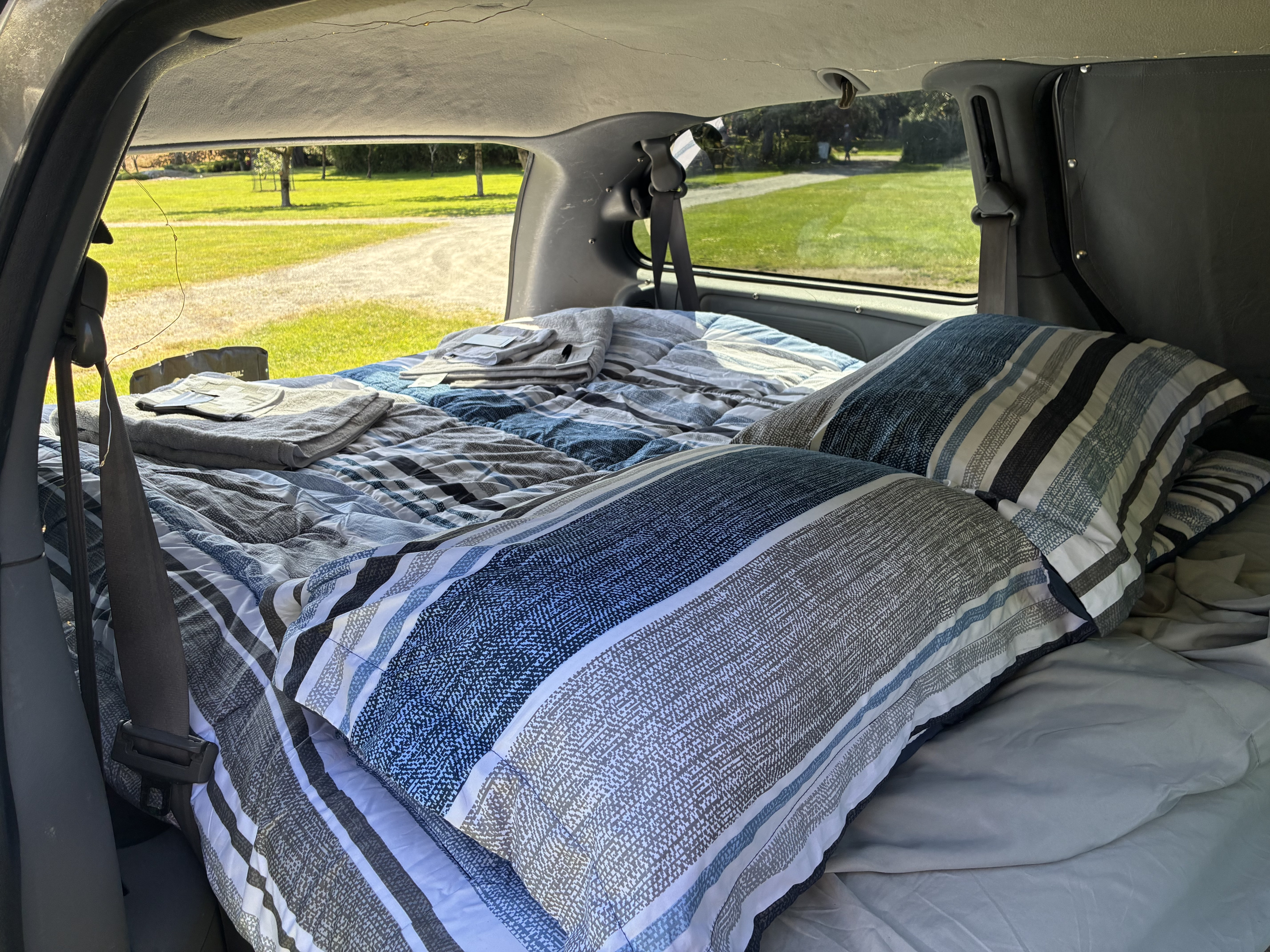 Inside a cozy RV rental: a comfy bed with striped pillows & blankets, ready for your next road trip adventure.. Dodge Grand Caravan 2005