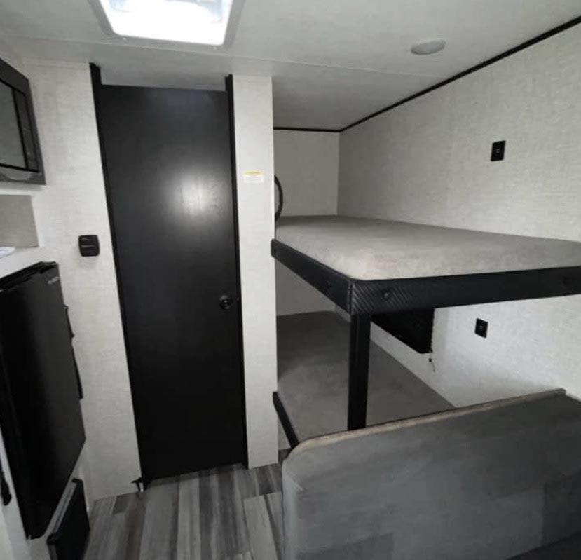 RV rental interior: bunk beds, a black door, small fridge, and microwave. Cozy space for travel adventures.. Jayco Jay Flight SLX 2025