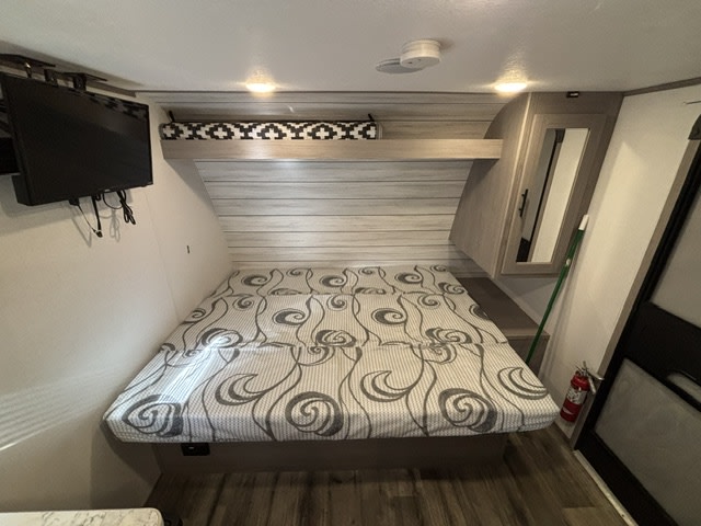Cozy RV rental bedroom with a large patterned bed, wall-mounted TV, and mirrored closet. Ready for a comfy road trip!. Dutchmen Coleman Lantern LT 2024