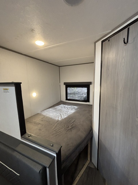 RV rental interior: A compact bedroom with a plush bed, window, overhead light, and nearby closet, ideal for travelers.. Dutchmen Coleman Lantern LT 2024