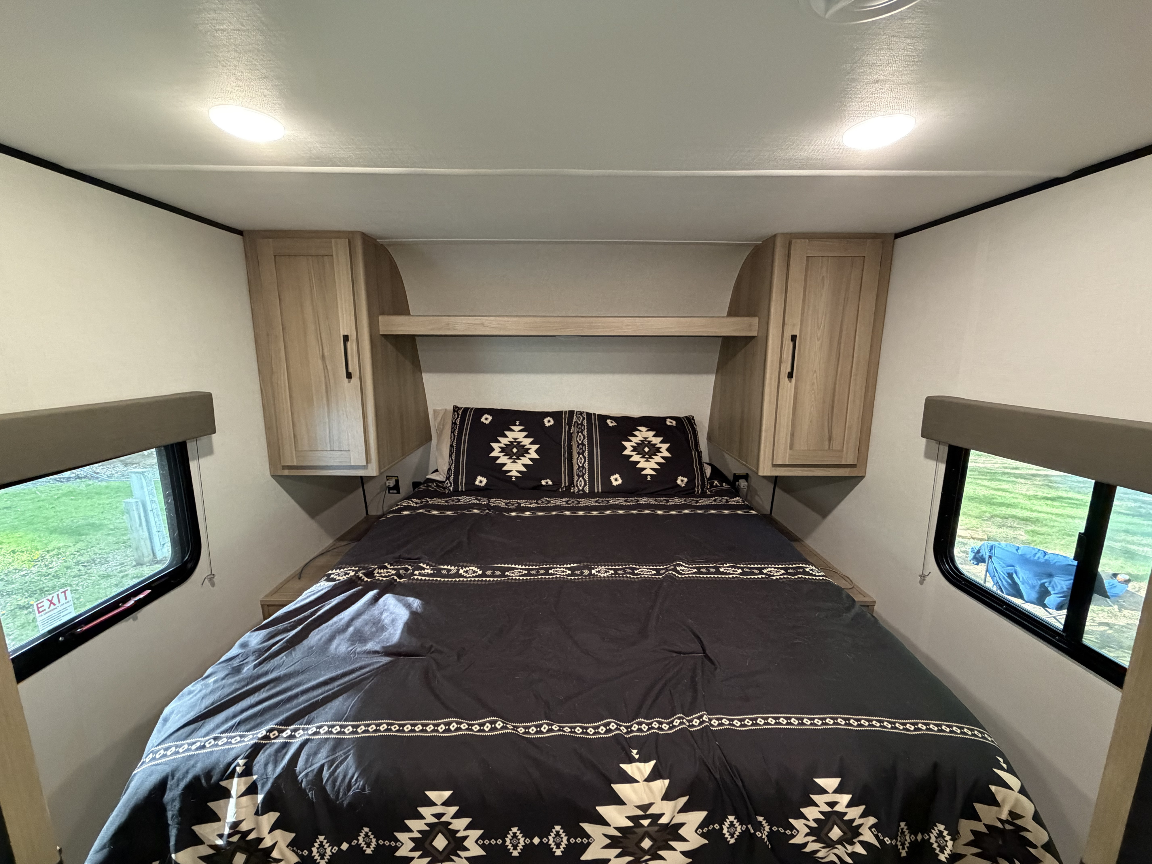 RV rental bedroom: a cozy interior with patterned bedding, overhead cabinets, and windows, offering comfortable sleeping in a travel trailer.. Keystone RV Coleman Light 2025