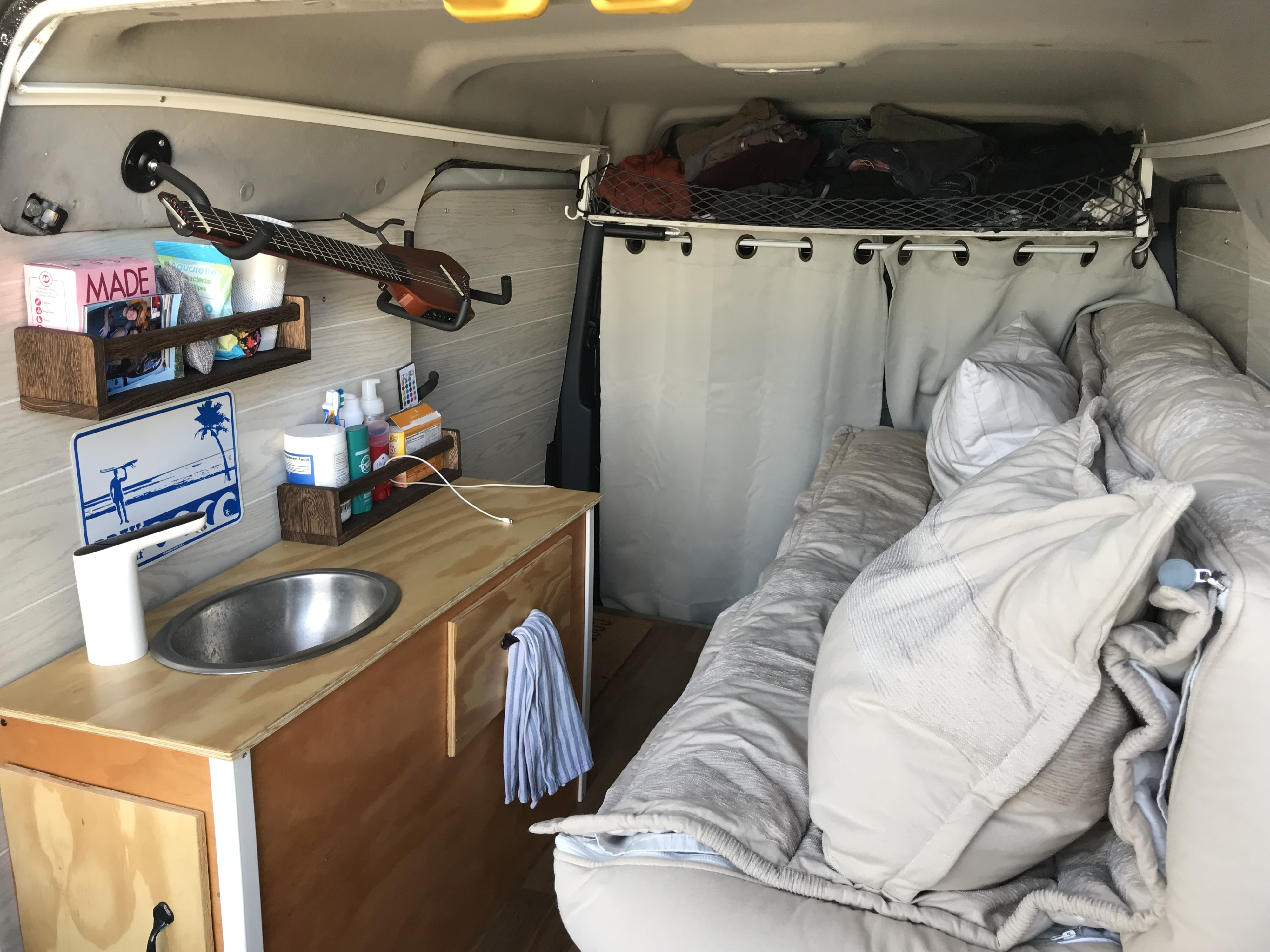 Inside an rv rental camper van: kitchenette with sink, cozy bed, shelves, guitar, & overhead storage for efficient living.. Ford Transit 2011