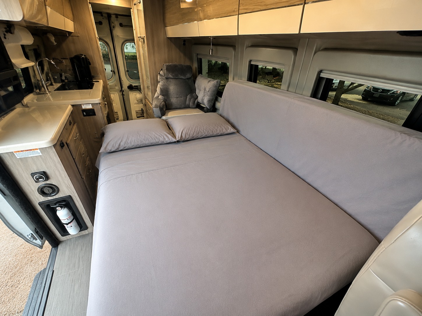 Spacious RV rental interior with a neatly made bed, kitchenette, and passenger seat. Fire extinguisher visible for safety.. Thor Sequnce 2023