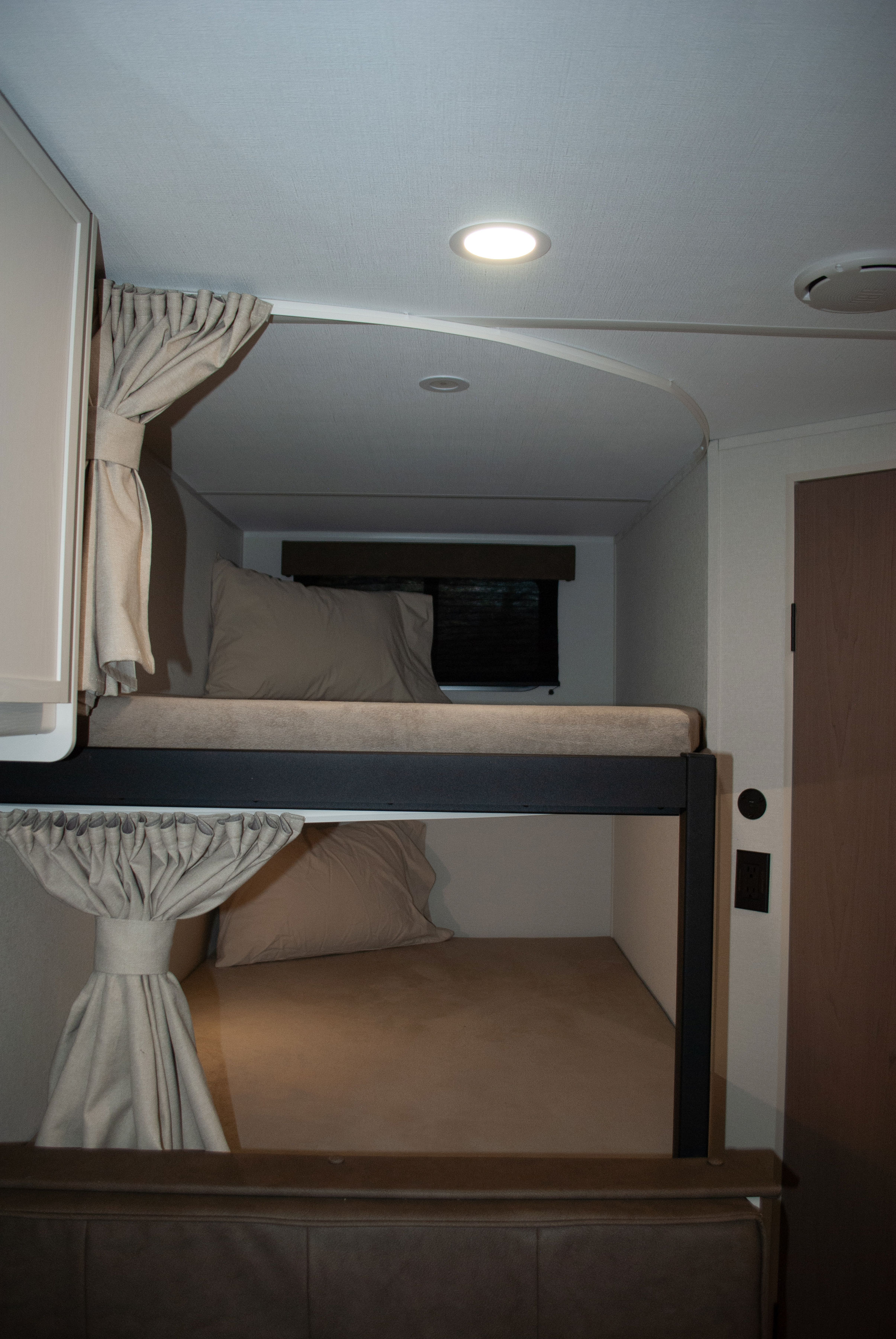 Inside an rv rental, cozy bunk beds with privacy curtains provide comfortable sleeping. Features include ceiling lighting and wall outlets.. Grand Design Transcend Xplor 2026