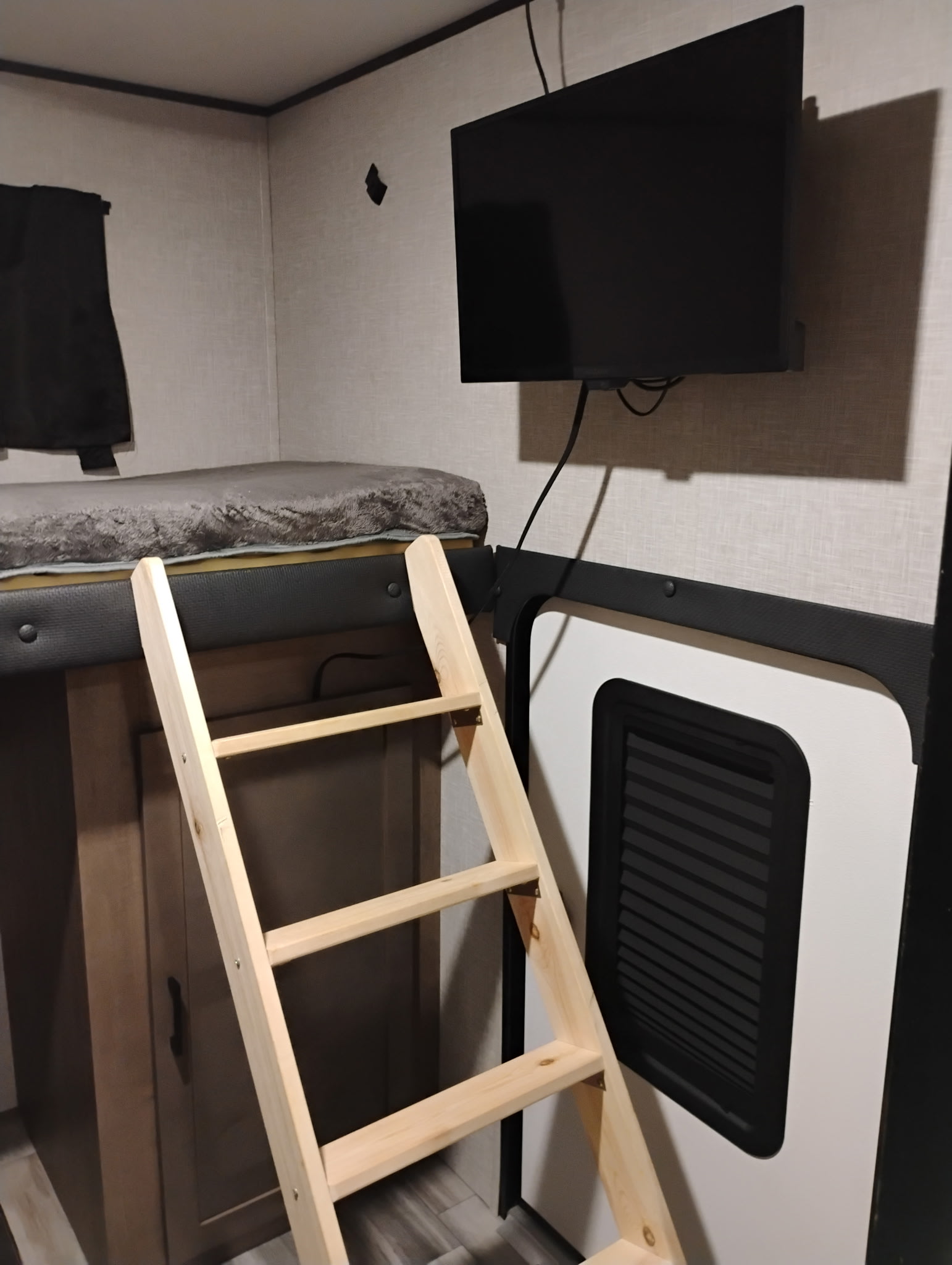 Inside an RV rental: a wooden ladder leads to a cozy bunk bed, with a wall-mounted TV and cabinet below.. Jayco Jay Flight SLX 2024