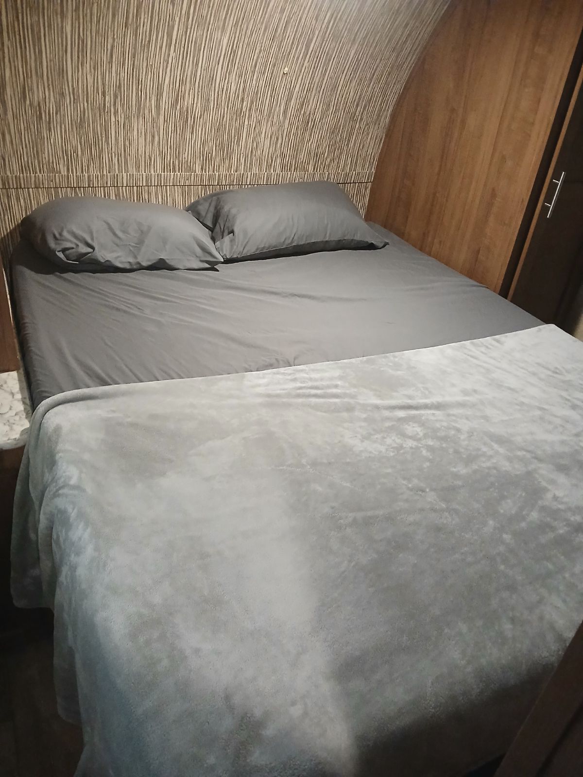 Experience comfort in this RV rental: a cozy bed with gray sheets, plush blanket, and unique textured headboard.. Gulf Stream Innsbruck 2019