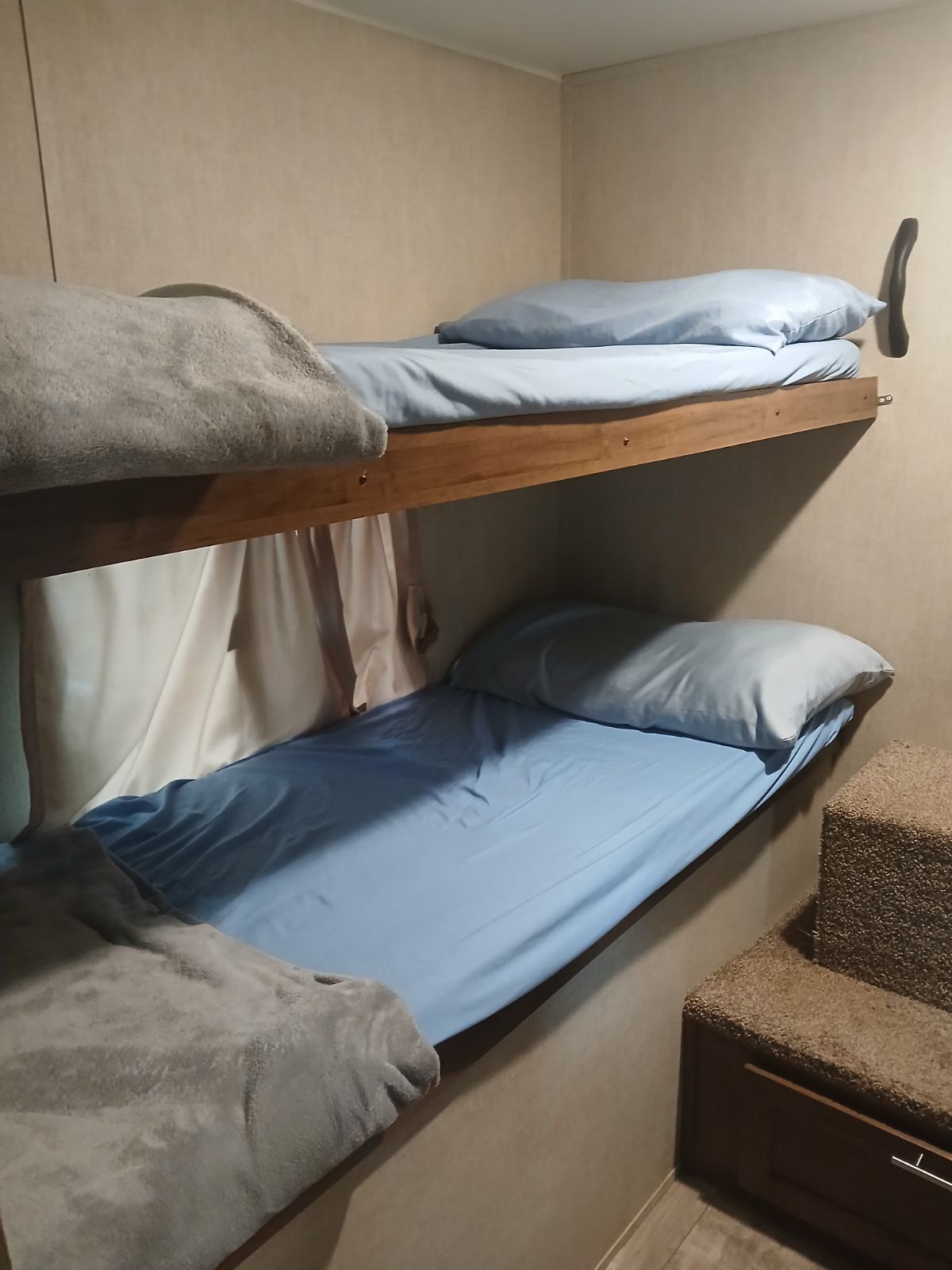 This RV rental features stacked bunk beds with blue sheets and cozy gray blankets. Carpeted steps on the right offer compact sleeping space.. Gulf Stream Innsbruck 2019