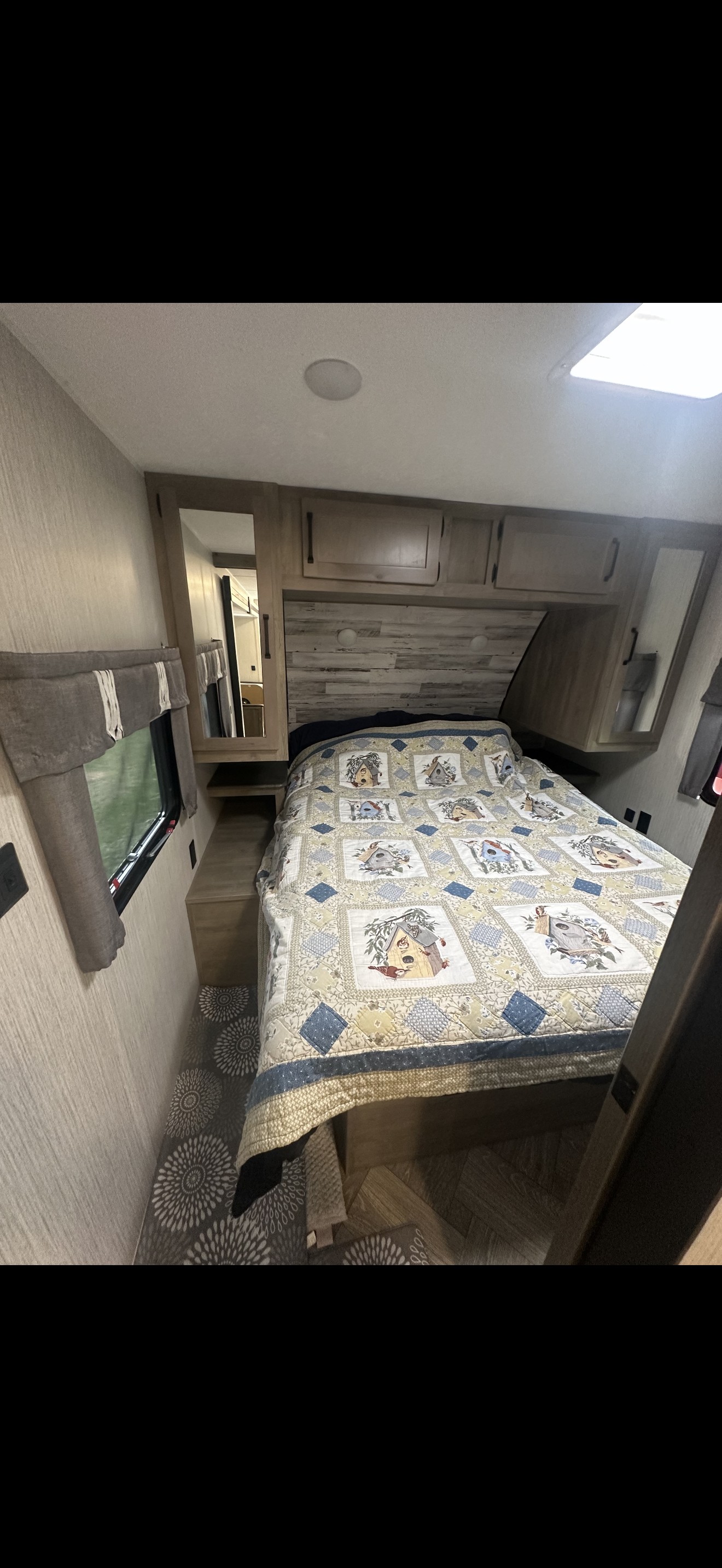 Cozy RV rental bedroom featuring a bed with a detailed birdhouse quilt, overhead storage, mirrored closets, and a window.. Forest River Palomino Puma 2022