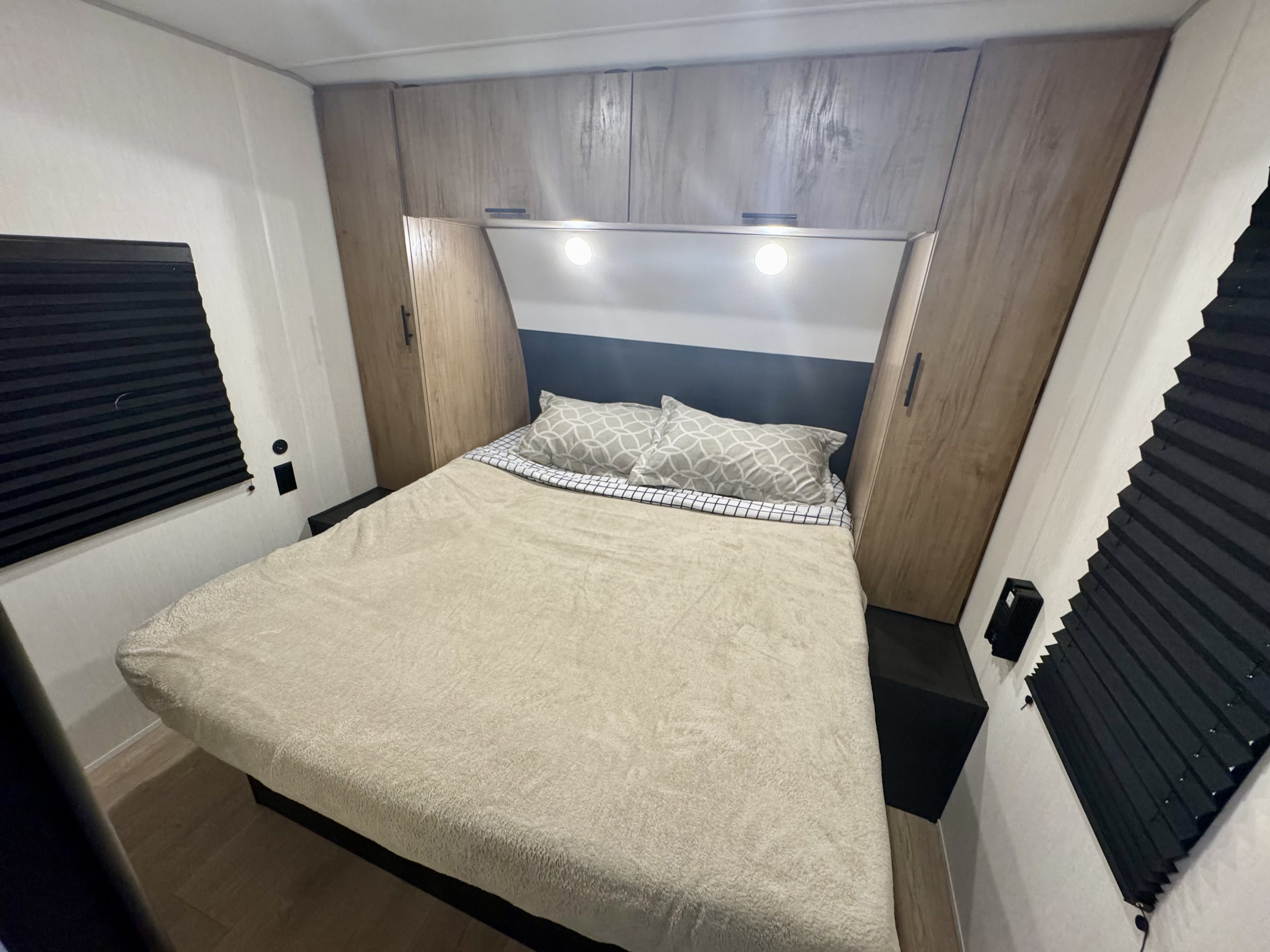 Inside an RV rental, a compact bedroom with a bed, overhead cabinets, bedside shelves, and blackout blinds.. Forest River Cherokee Grey Wolf 2025