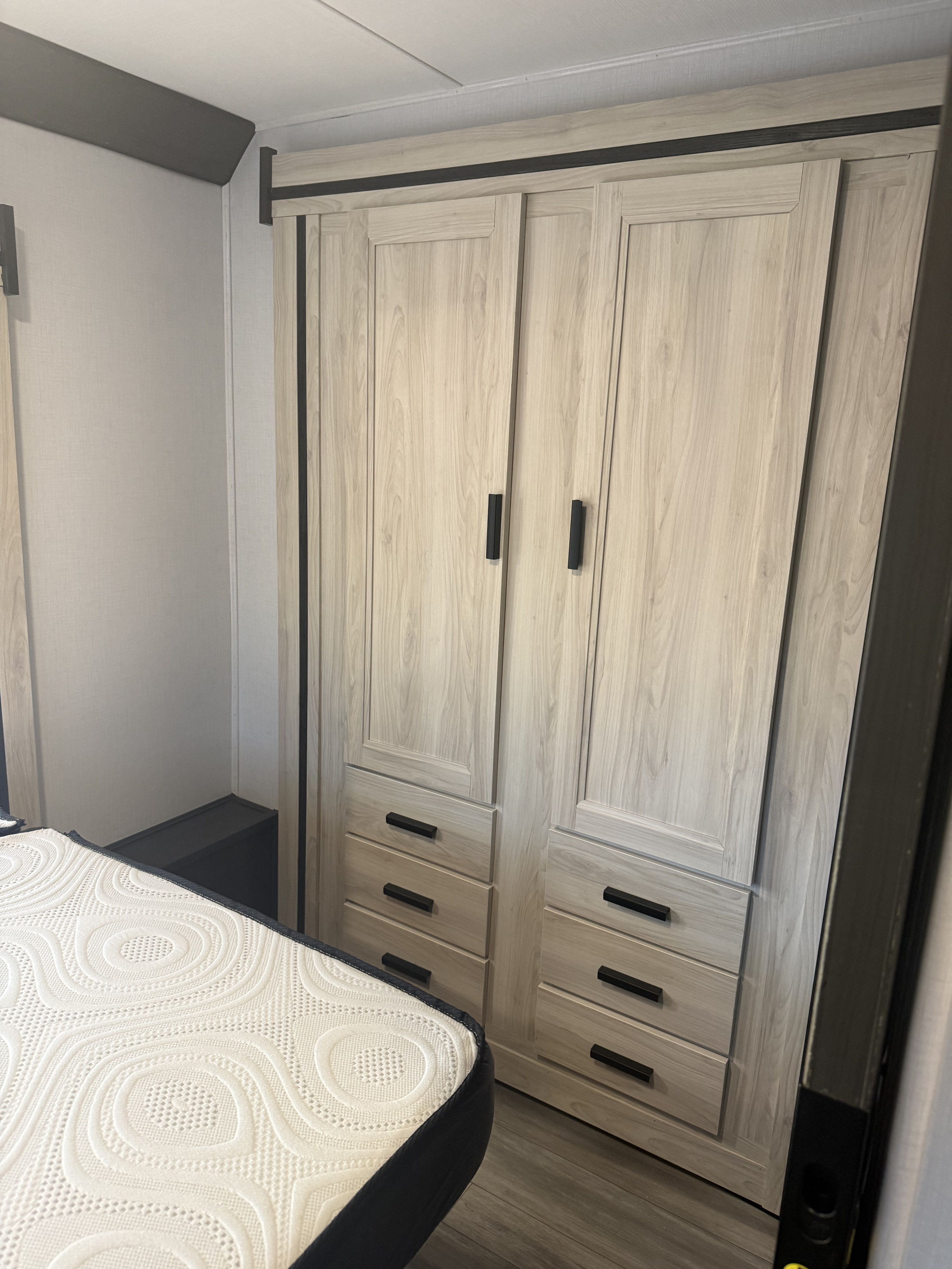 Inside an RV rental: a modern bedroom featuring a light wood wardrobe with multiple drawers and a white textured mattress.. Forester 2501CD 2023